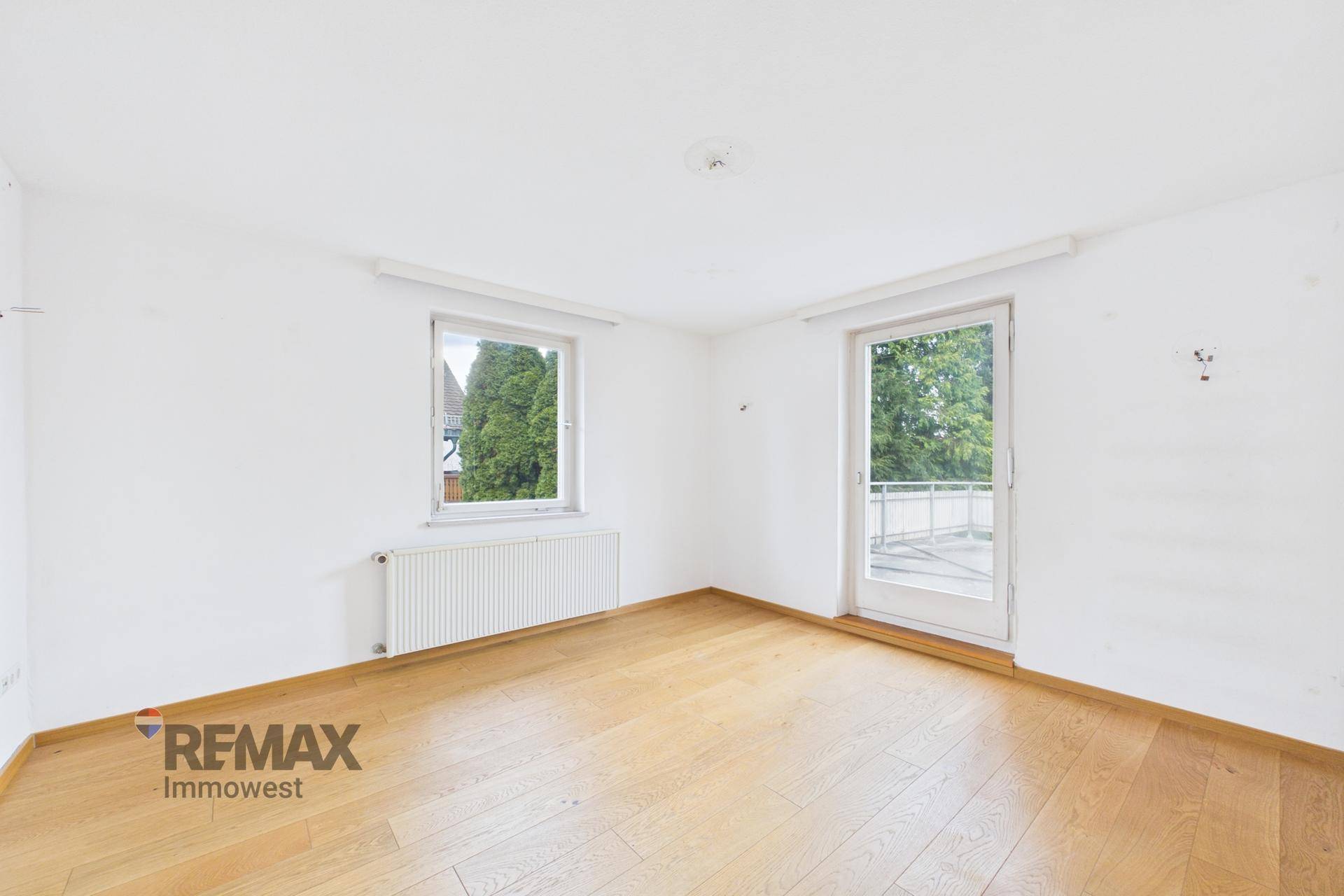 Helles Schlafzimmer mit Parkettboden und Zugang zu einem Balkon, viel Tageslicht.
