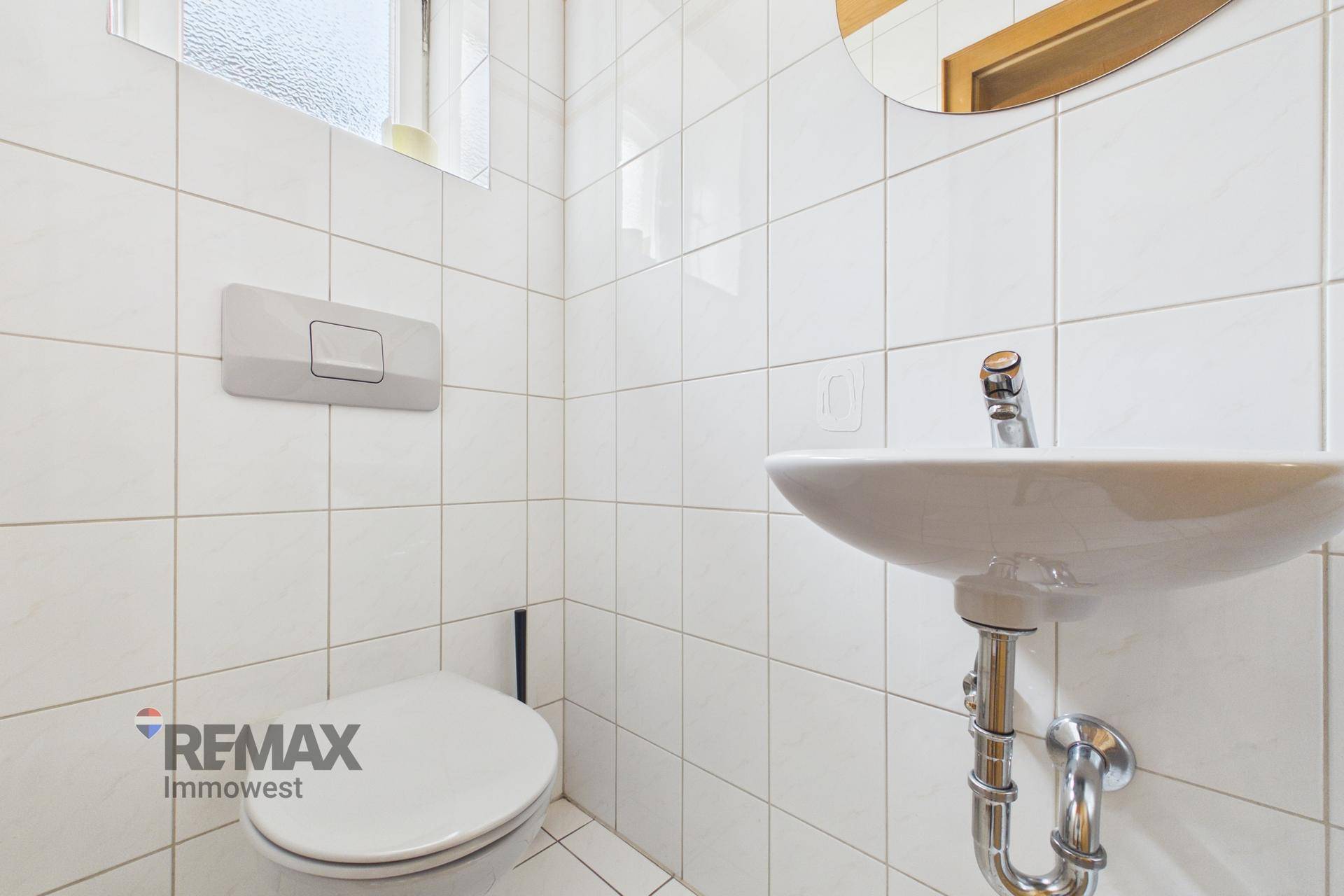 Kleines Gäste-WC mit weißen Fliesen, Toilette und Waschbecken.