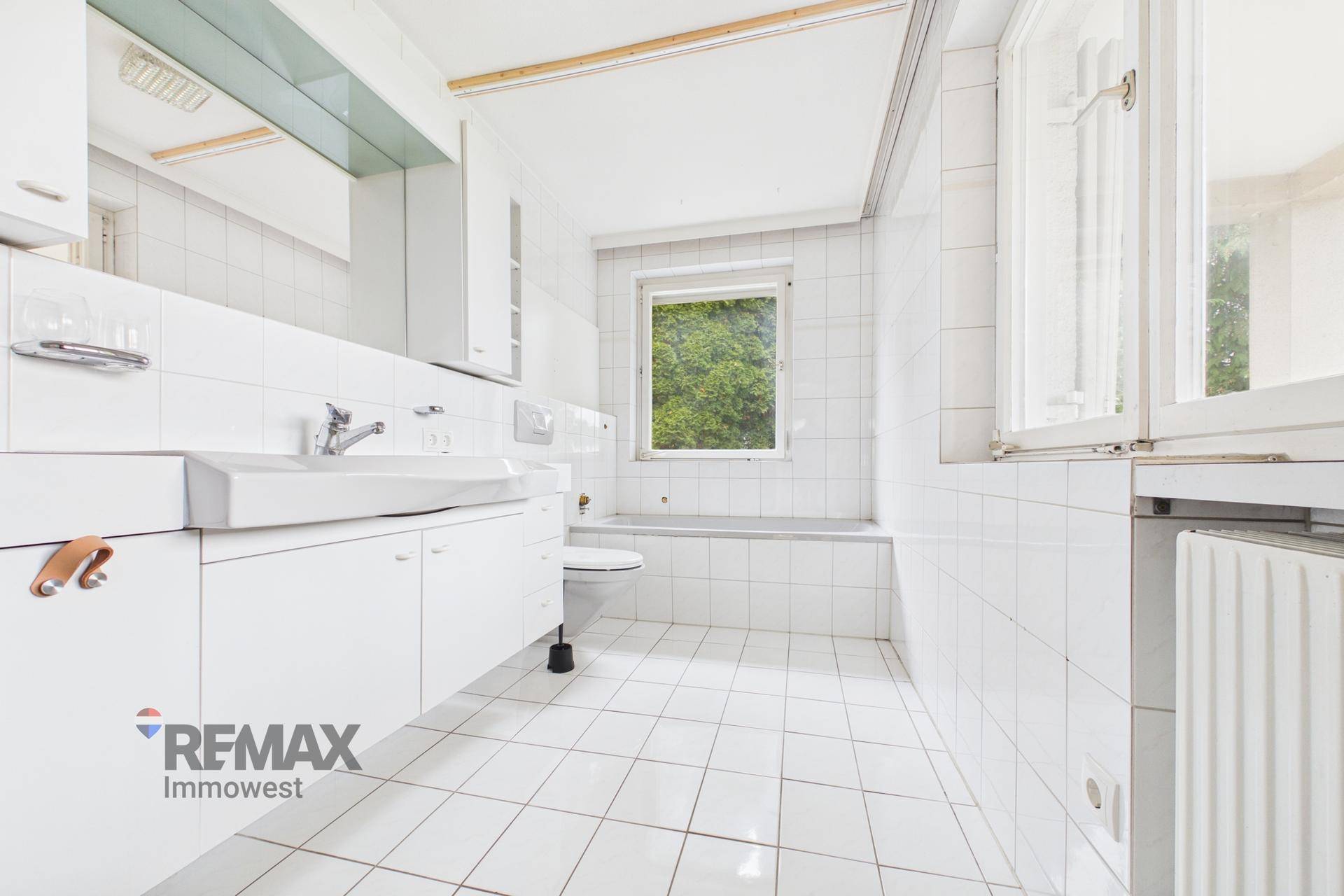 Helles Badezimmer mit weißen Fliesen, Badewanne und Fenster für Tageslicht.