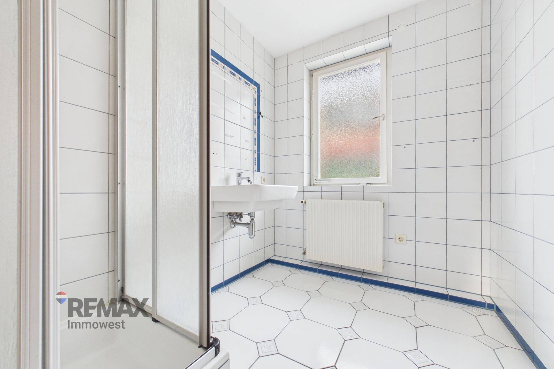 Badezimmer mit weißen Fliesen, Duschkabine und Fenster für natürliche Belüftung.