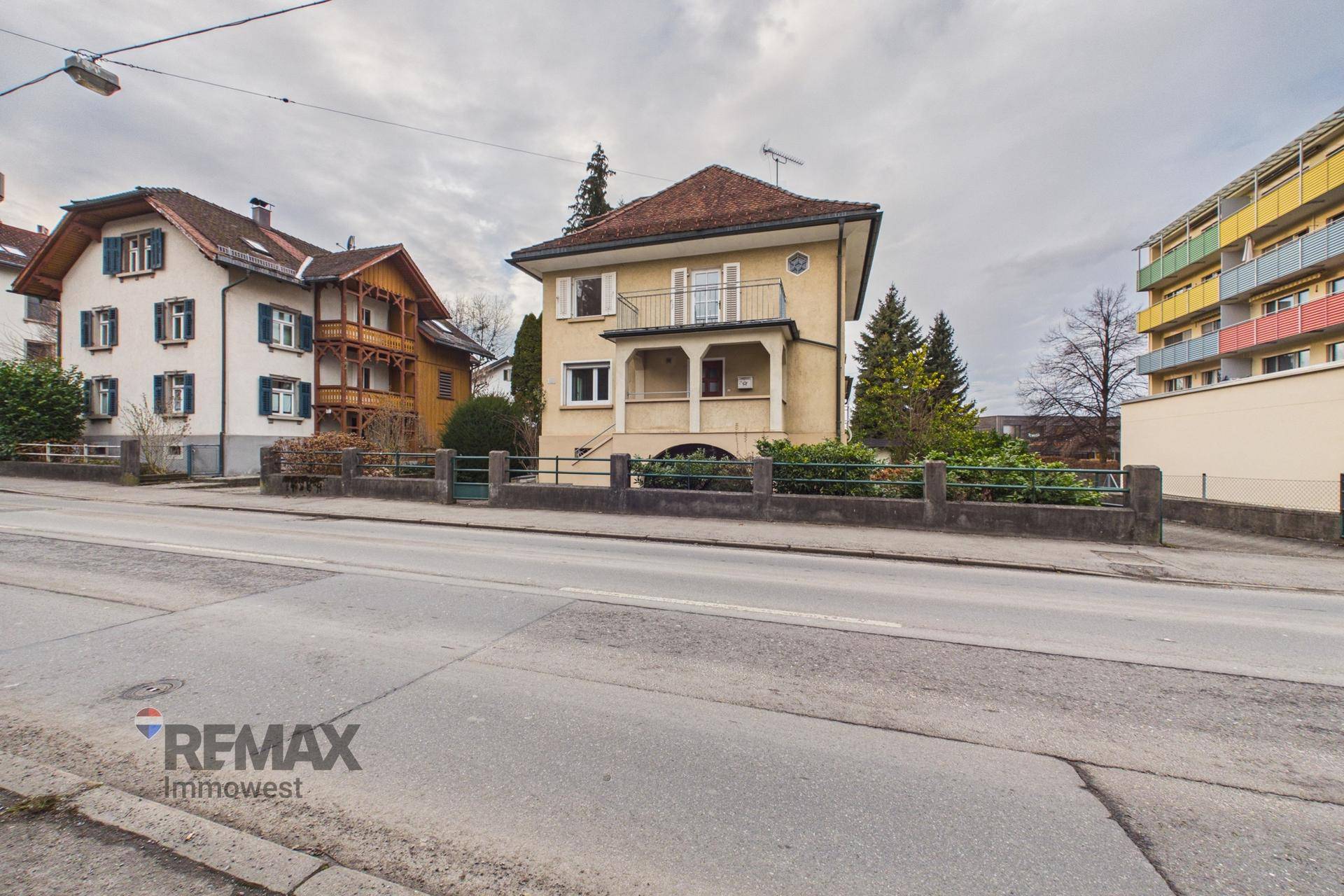 Ansicht des Hauses von der Straße, umgeben von anderen Gebäuden und Bäumen.