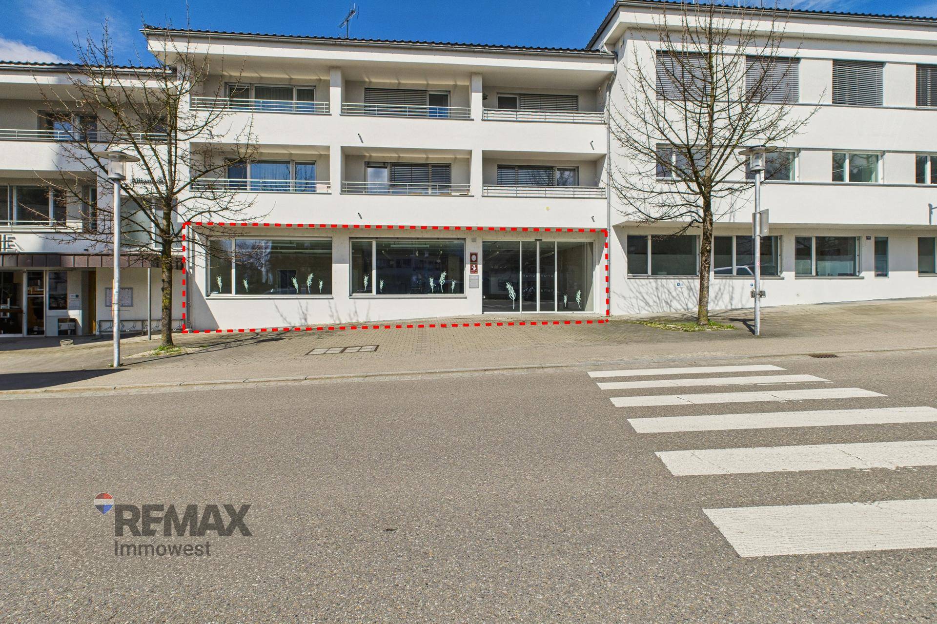 Ansicht des Geschäftsgebäudes von der Straße mit breiten Schaufenstern und einem Zebrastreifen davor.