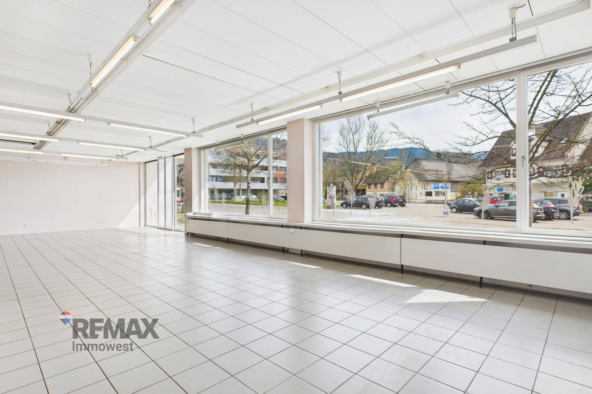 Geräumiger Verkaufsraum mit durchgehenden Fensterfronten und weißem Fliesenboden.