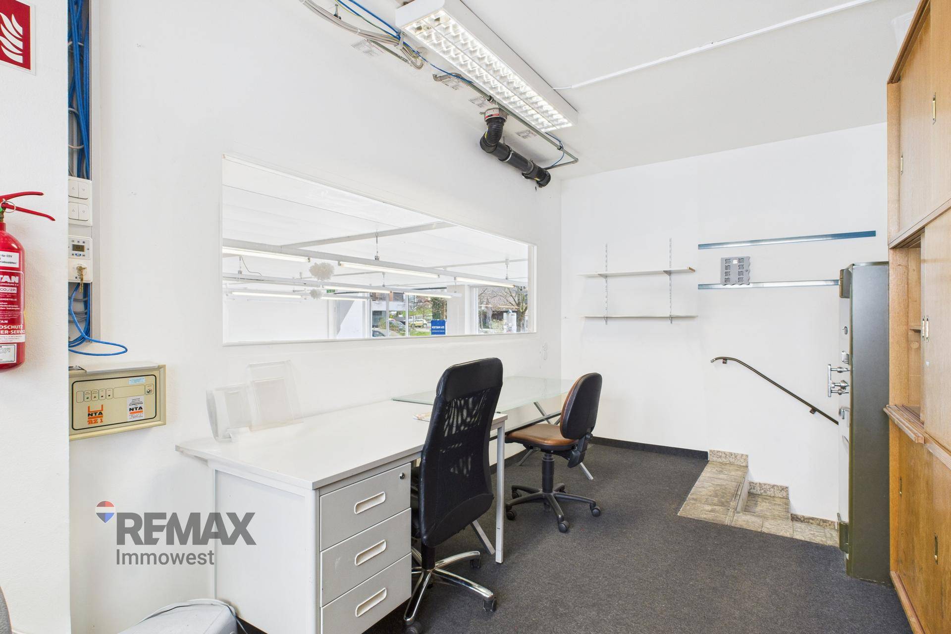Bürobereich mit Schreibtisch, Bürostühlen und einem Fenster, das Tageslicht hereinlässt.