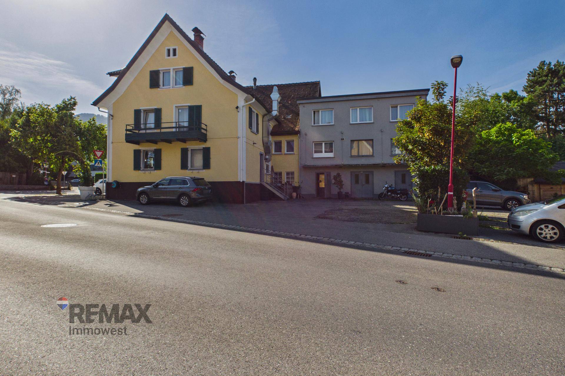 Gelbes Gebäude mit traditioneller Architektur und einem grauen Anbau an einer Straßenecke.