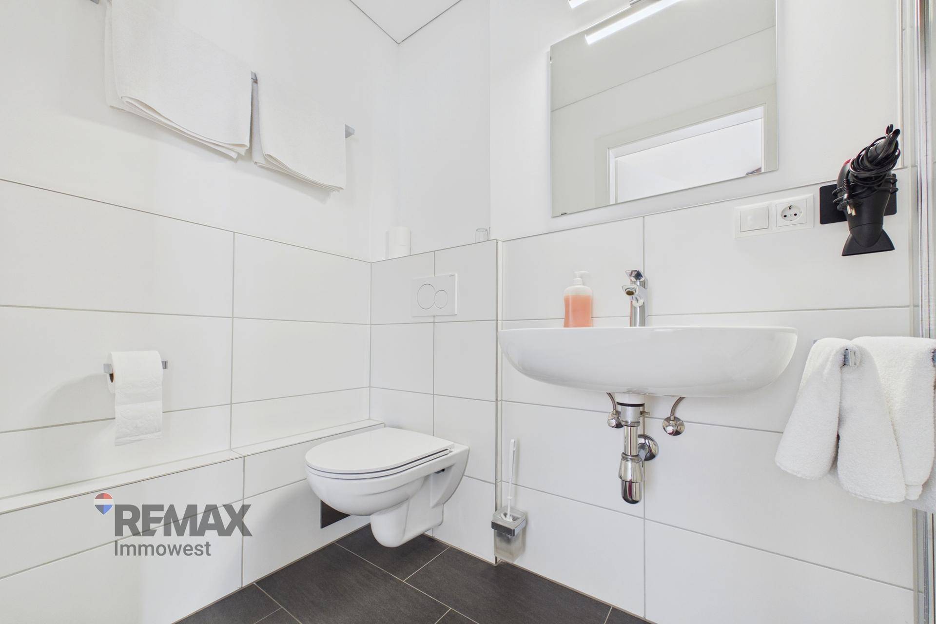 Modernes Badezimmer mit weißen Fliesen, wandhängendem WC und Waschbecken, sehr sauber und funktional.