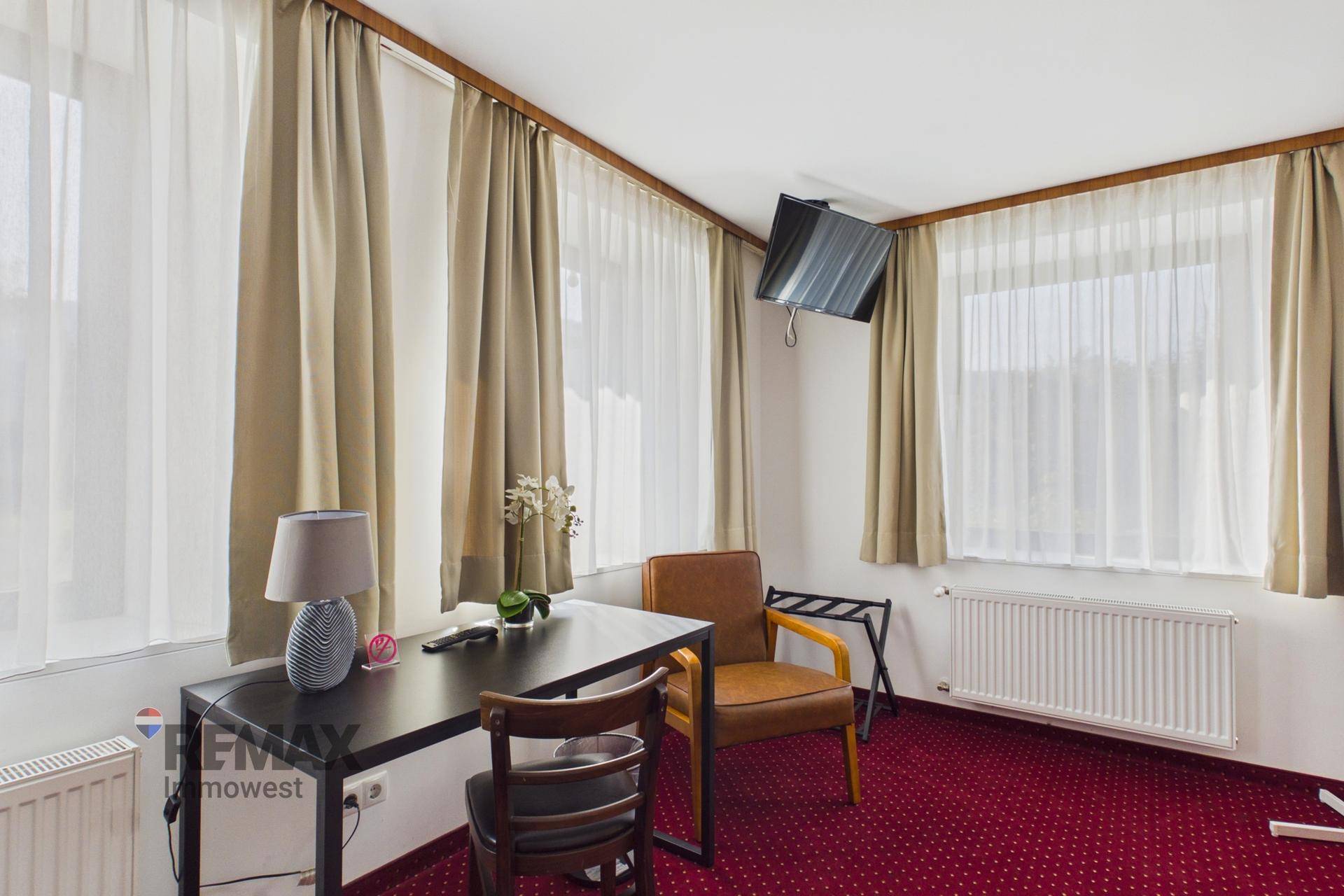 Helles Schlafzimmer mit zwei großen Fenstern, Schreibtisch und Fernseher, ideal für Gäste.