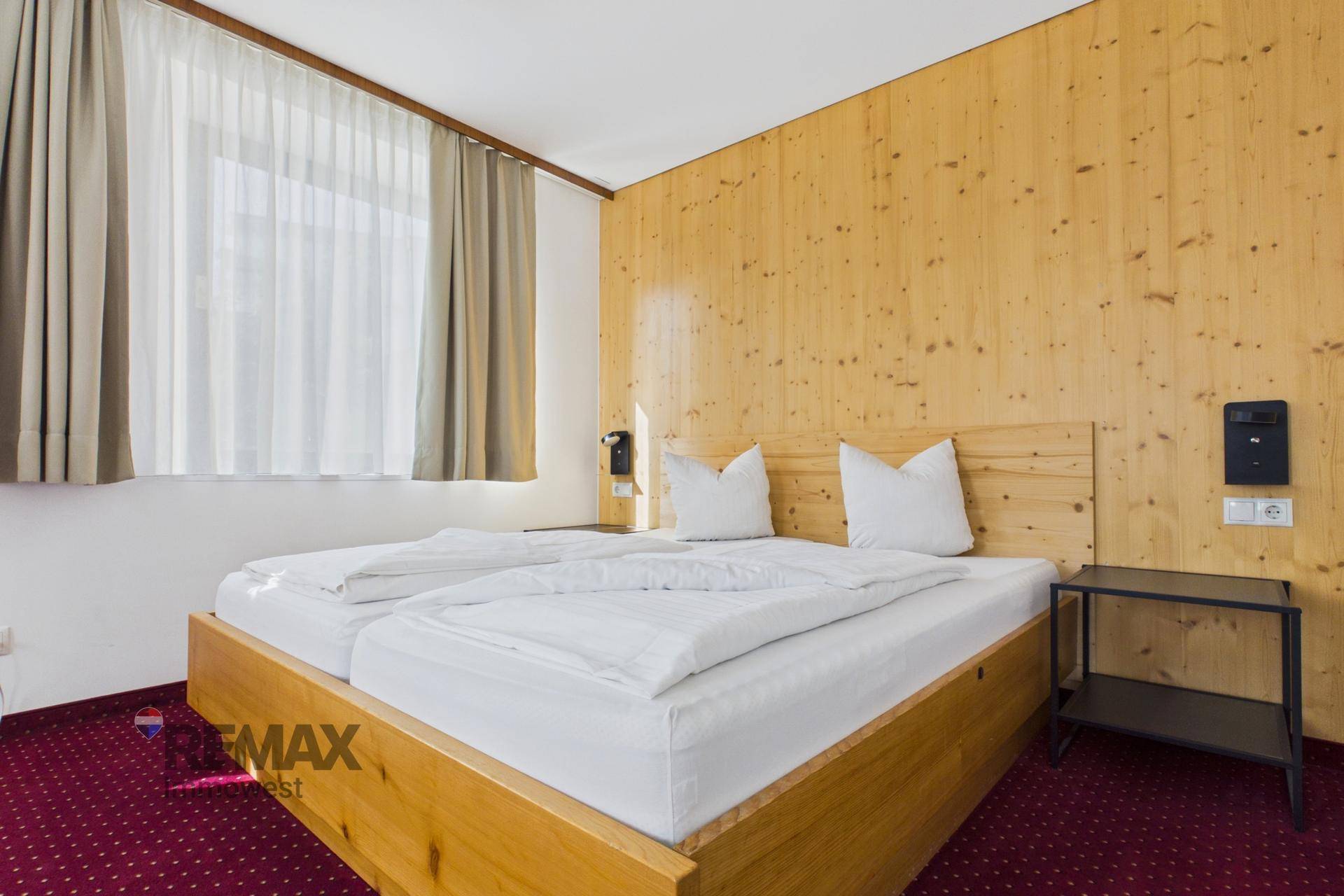 Gemütliches Schlafzimmer mit Holzwänden, Doppelbett und rotem Teppichboden, bietet eine warme Atmosphäre.