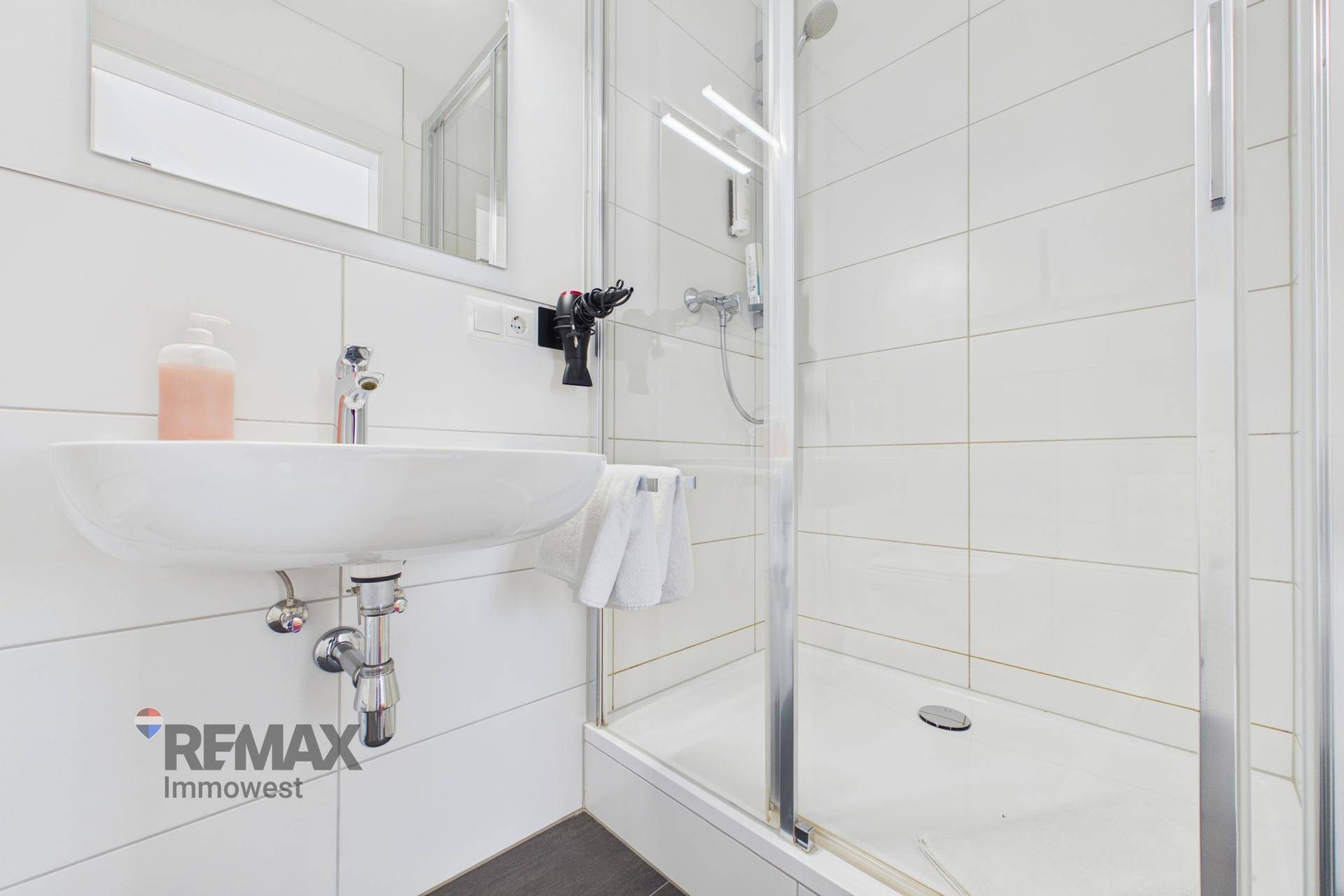 Modernes Badezimmer mit Duschkabine, Waschbecken und weißen Fliesen, sehr sauber und hell.