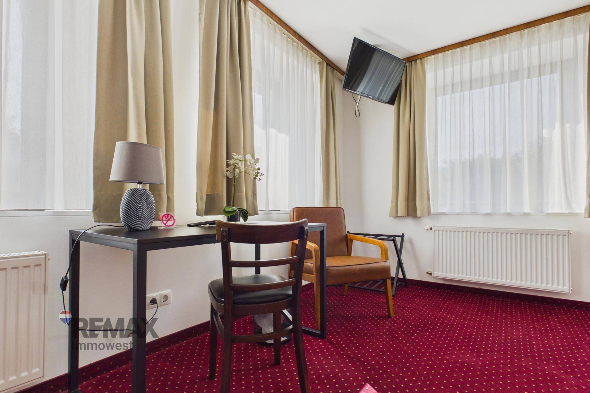 Helles Schlafzimmer mit zwei großen Fenstern, Schreibtisch und Fernseher, ideal für Gäste.
