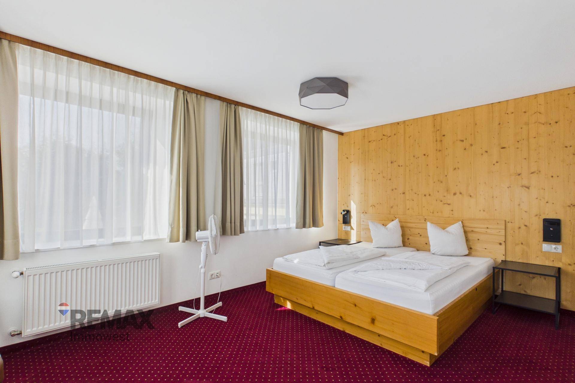 Geräumiges Schlafzimmer mit Holzwänden, Doppelbett und rotem Teppichboden, hell durch große Fenster.