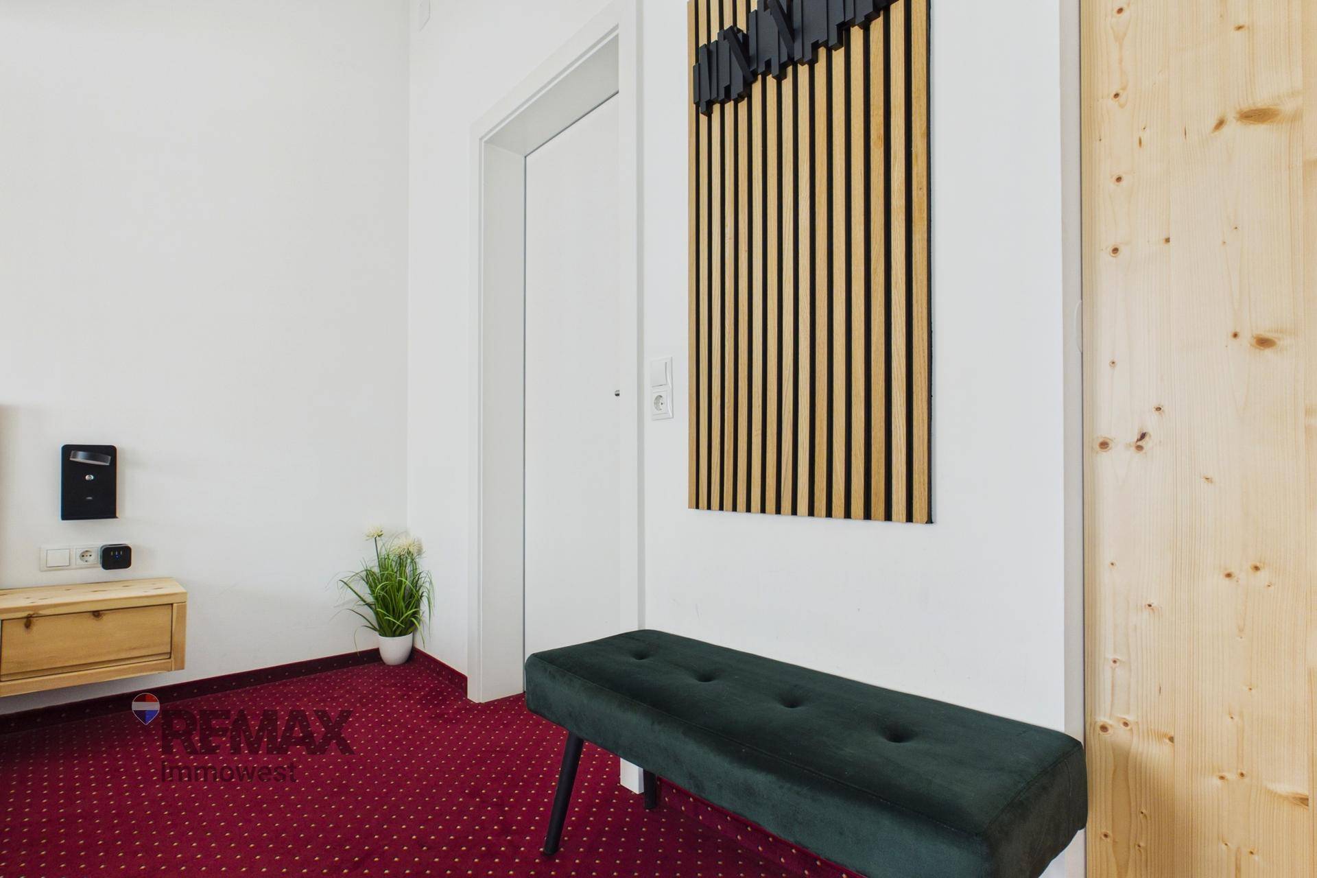 Heller Flur mit rotem Teppichboden, Holzwandverkleidung und einer modernen Sitzbank.