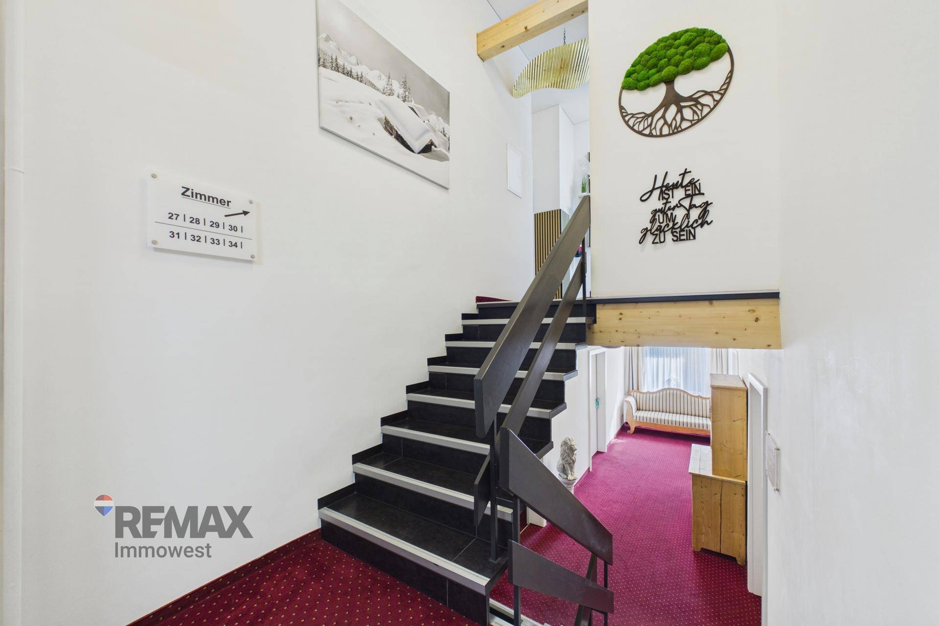 Treppenhaus mit dunklen Stufen und weißer Wand, geschmückt mit modernen Kunstwerken und Wegweisern.