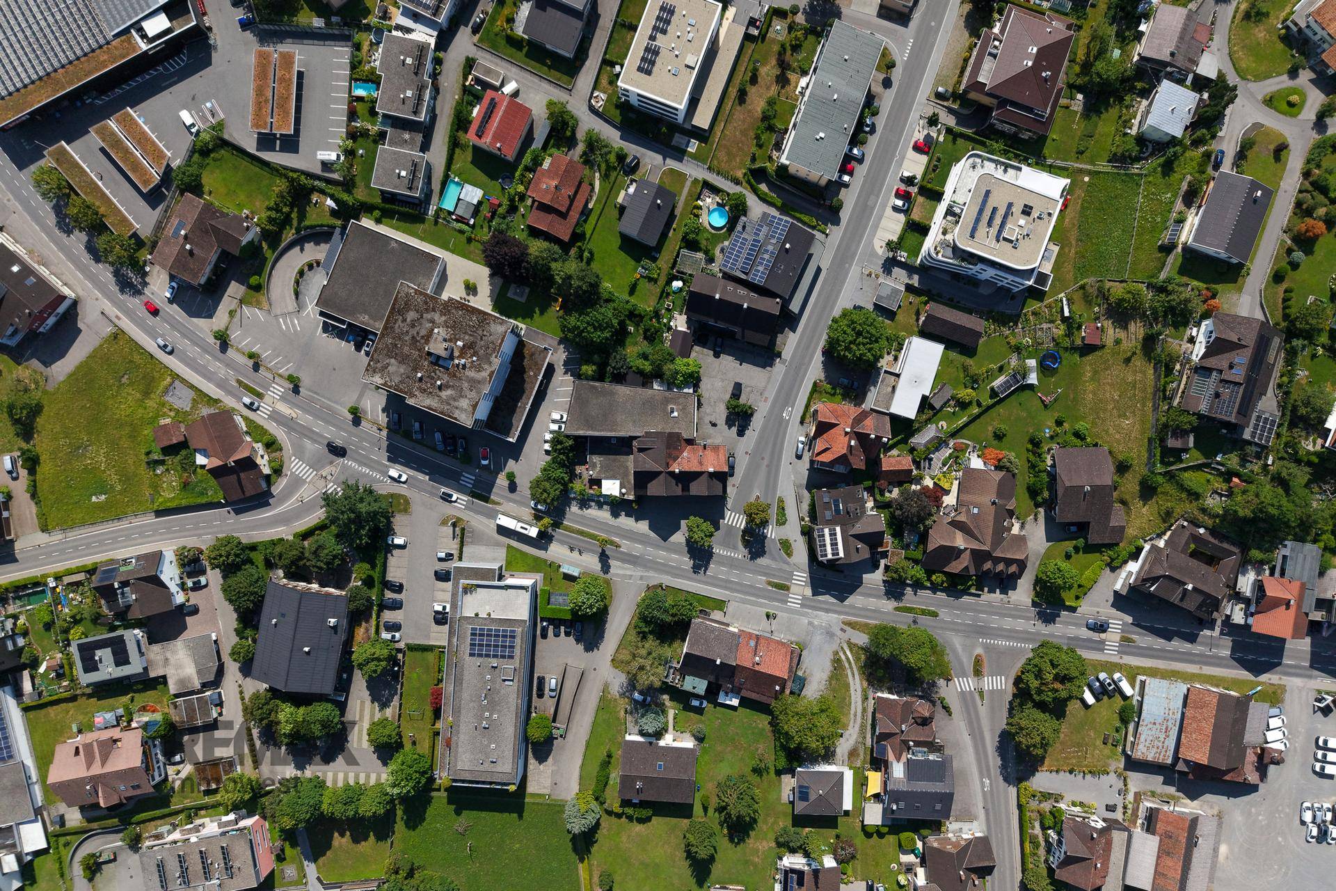 Luftaufnahme einer städtischen Siedlung mit verschiedenen Gebäuden, Straßen und Grünflächen unter klarem Himmel.