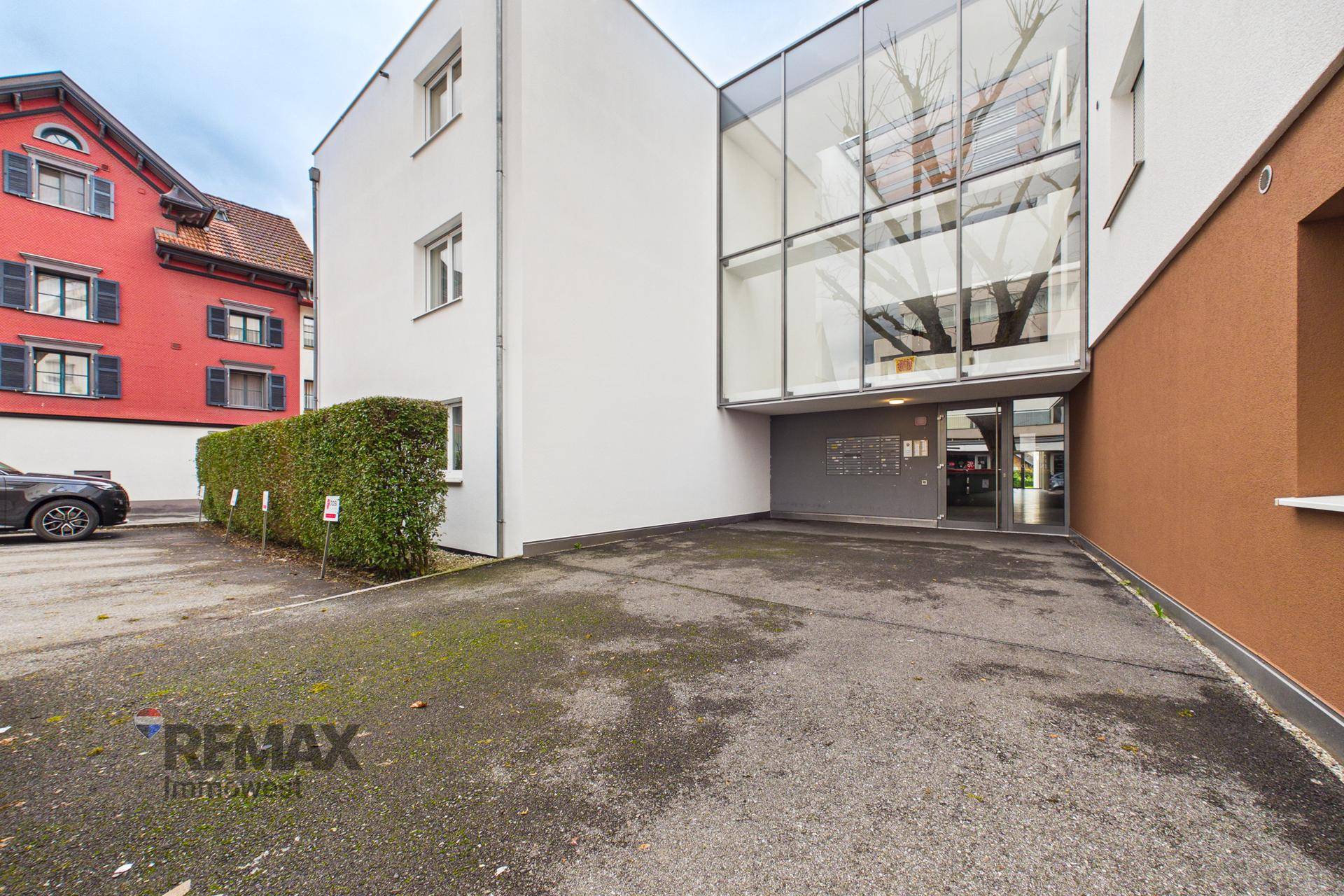 Moderne Gebäudefassade mit großer Glasfront am Eingangsbereich und Parkplätzen.