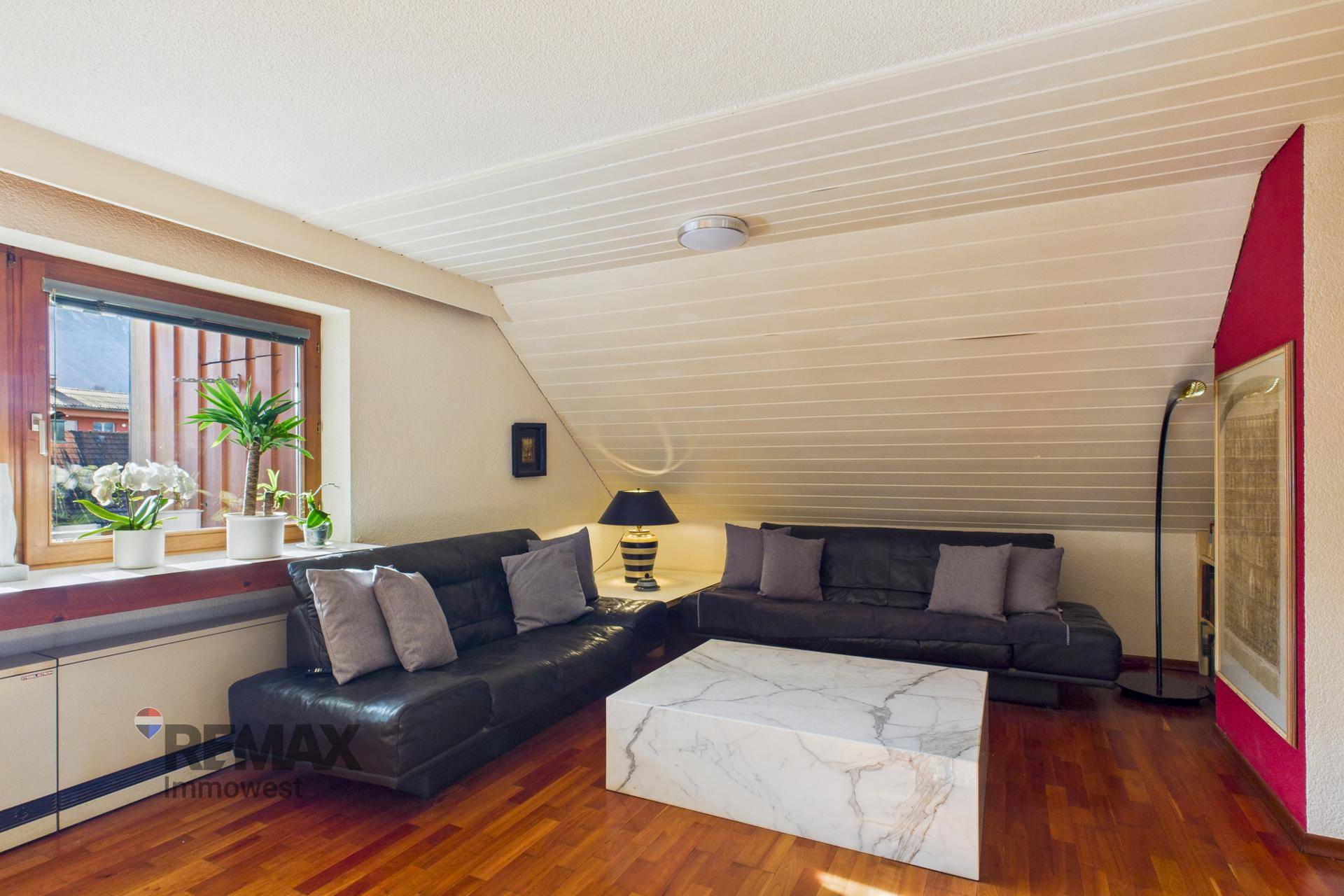 Gemütliches Wohnzimmer mit Holzboden, Dachschräge und großem Marmor-Couchtisch.