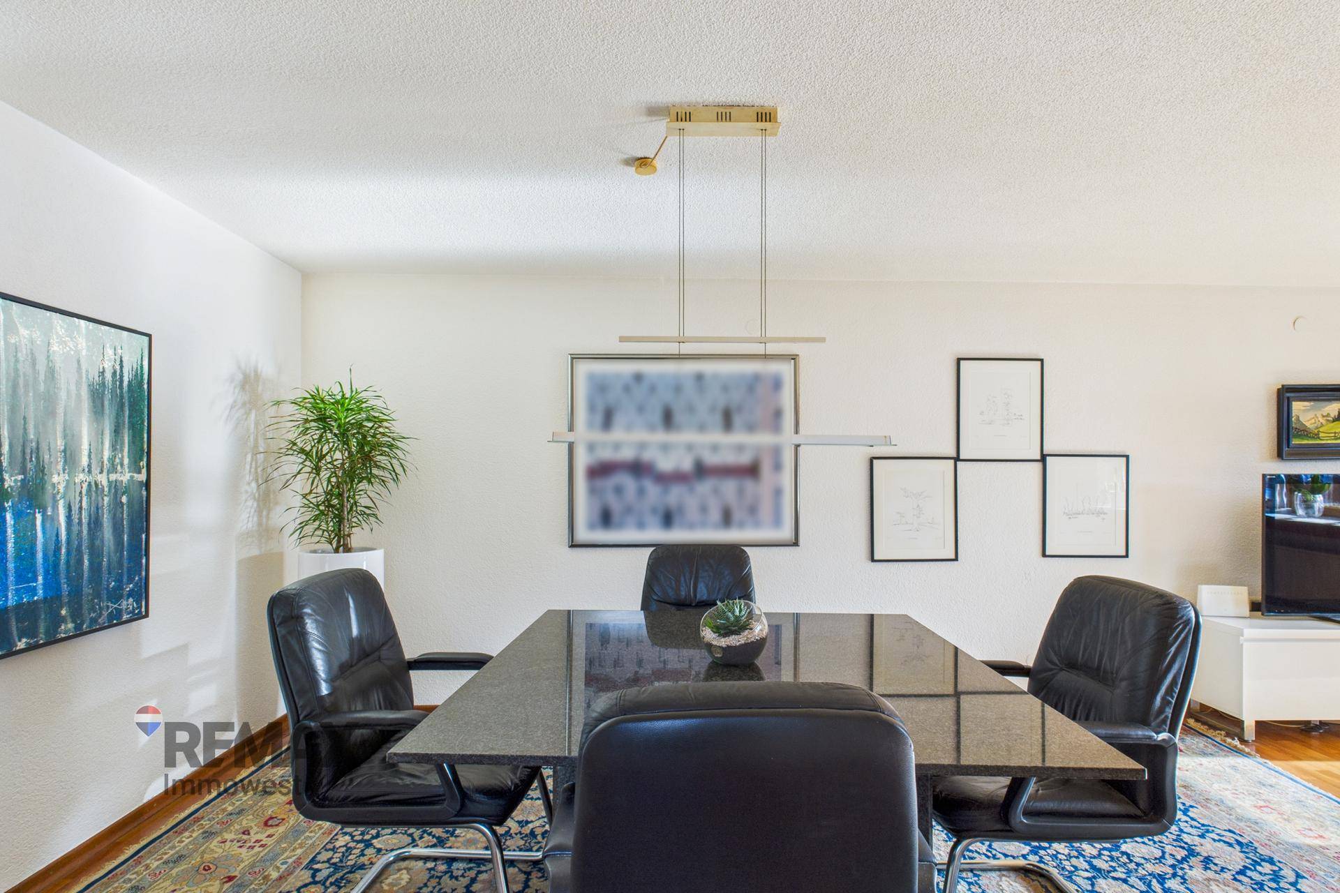 Essbereich mit dunklem Granittisch und Teppich, umgeben von hellen Wänden und Kunstwerken.