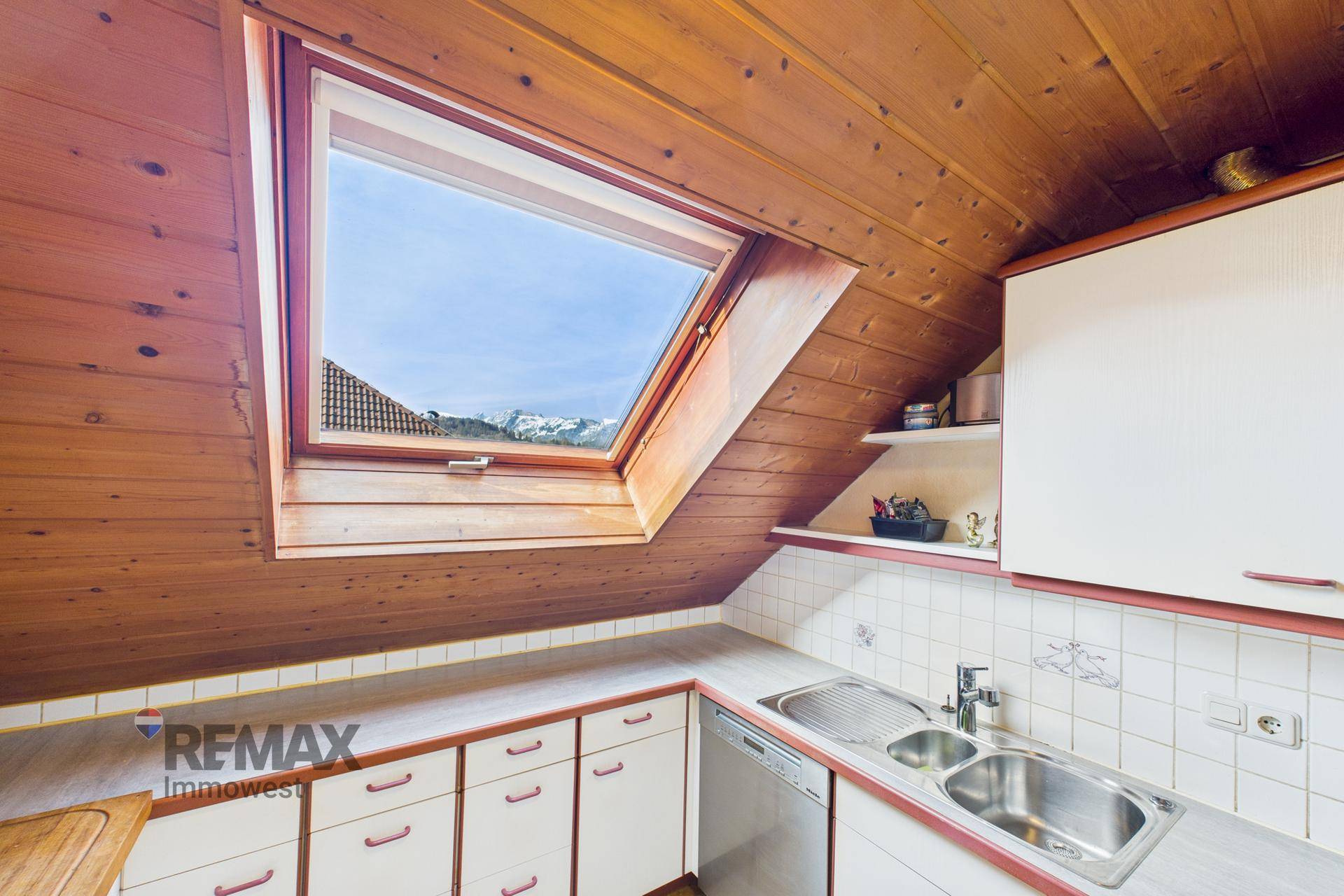 Küche im Dachgeschoss mit Holzverkleidung, Dachfenster und Bergblick.