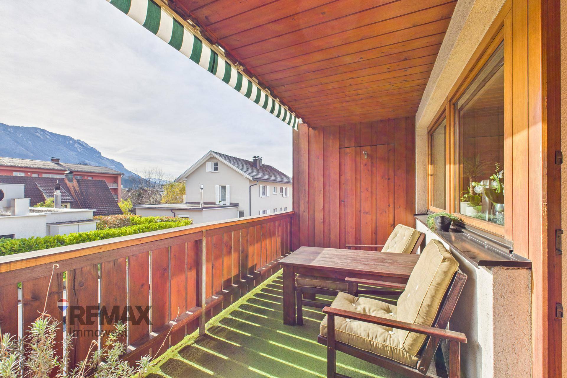 Geräumiger Holzbalkon mit Markise, Sitzgelegenheiten und Blick auf die Berge.