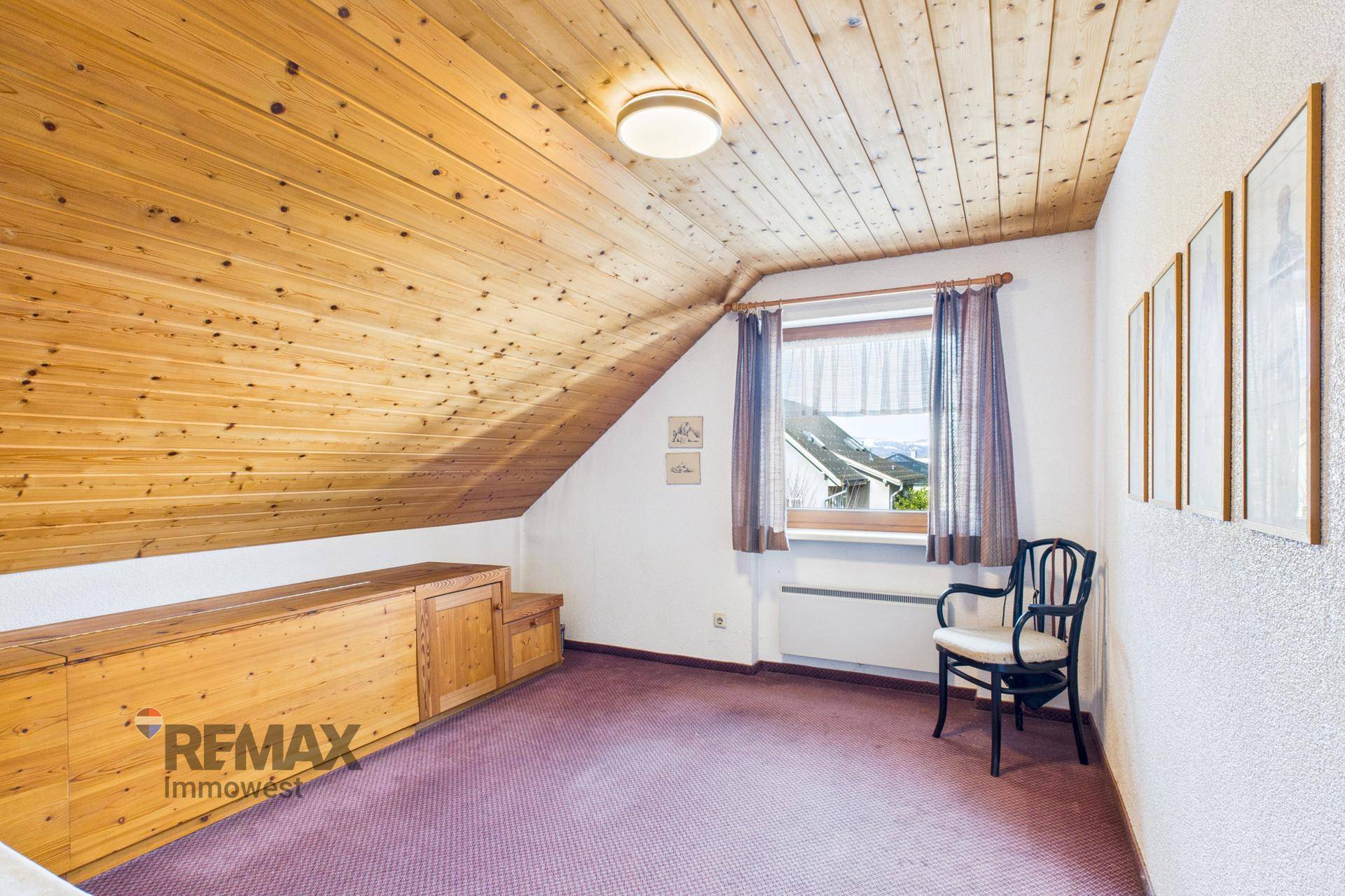 Schlafzimmer im Dachgeschoss mit Holzdecke, Teppichboden und eingebauten Holzmöbeln.