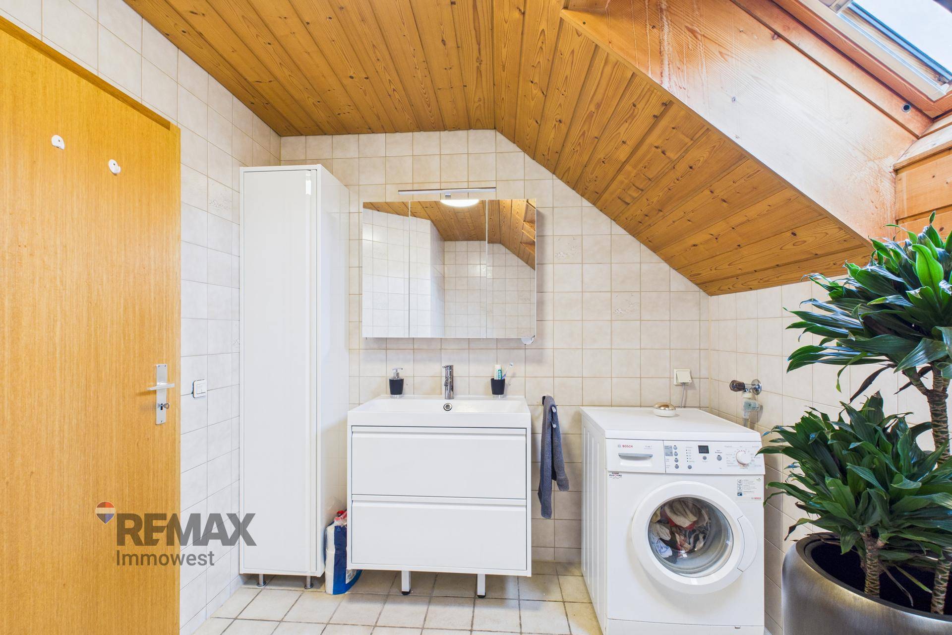 Badezimmer mit Waschbecken, Spiegelschrank, Waschmaschine und Dachschräge.