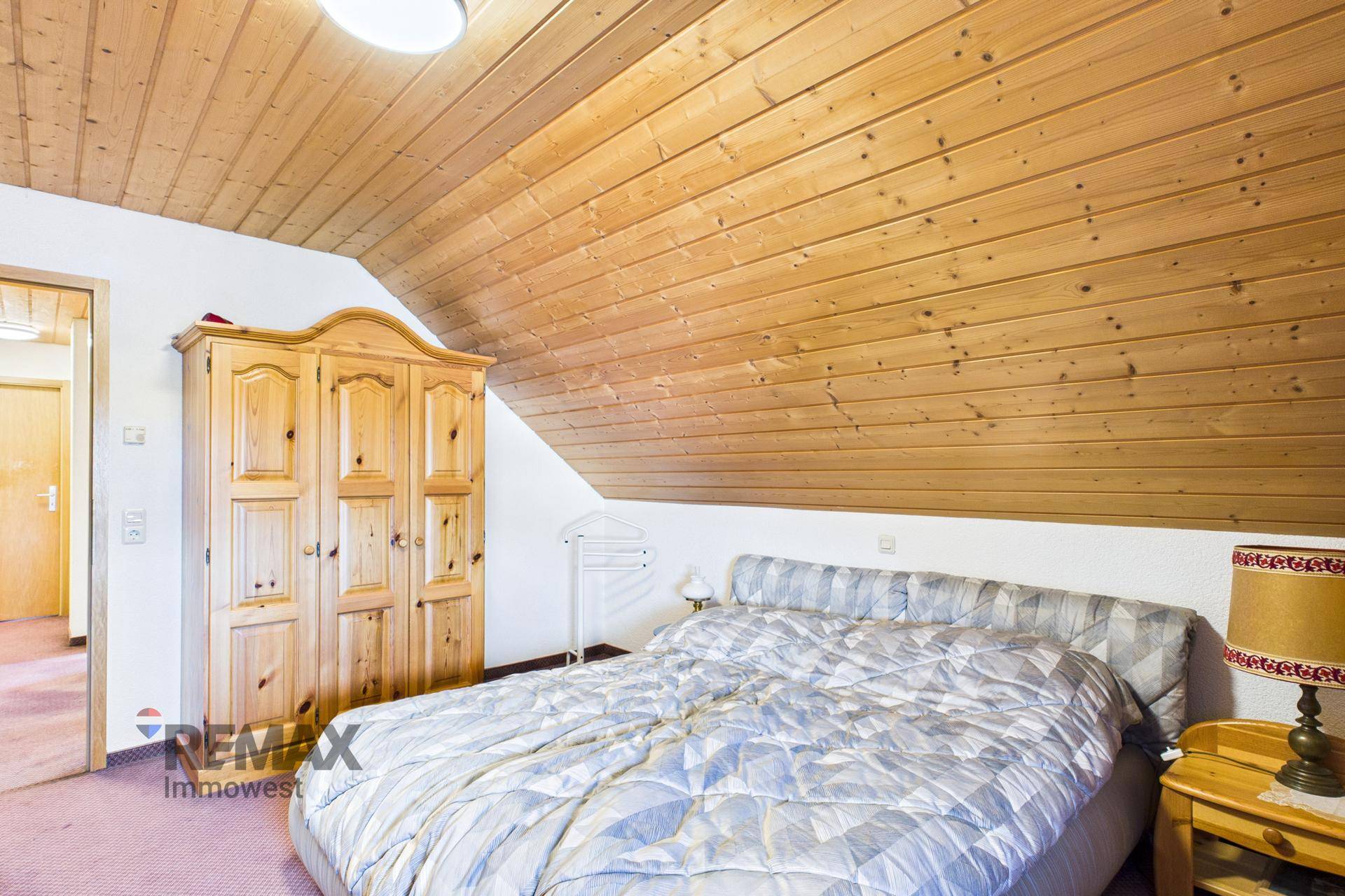 Gemütliches Schlafzimmer im Dachgeschoss mit Holzdecke, Teppichboden und Kleiderschrank.