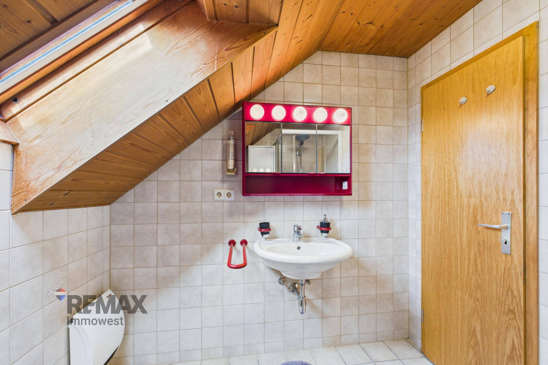Badezimmer mit Waschbecken, Spiegelschrank und Dachschräge, unter einer Holzdecke.