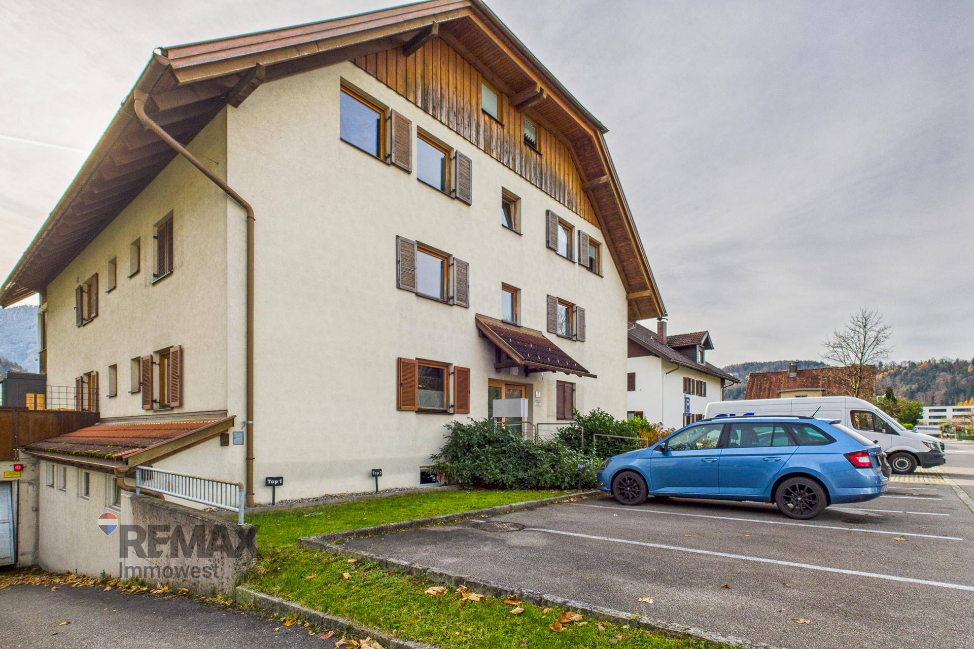 Mehrfamilienhaus mit Parkplätzen und Zugang zur Tiefgarage, umgeben von Grünflächen.