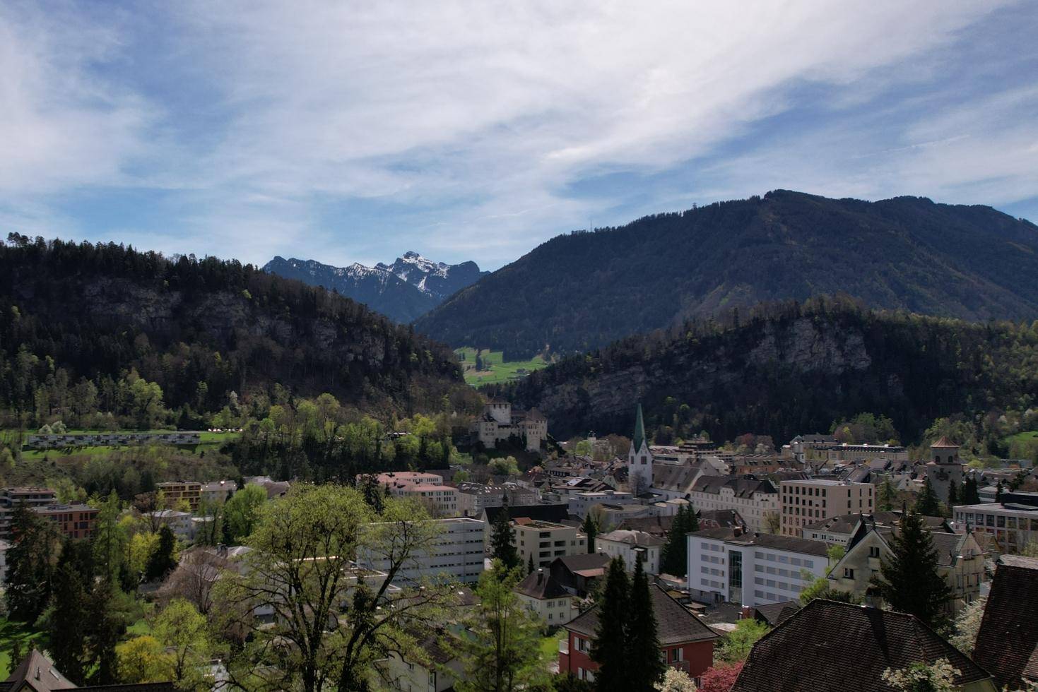 Panoramablick auf eine Stadt im Tal mit einer Kirche und schneebedeckten Bergen im Hintergrund.