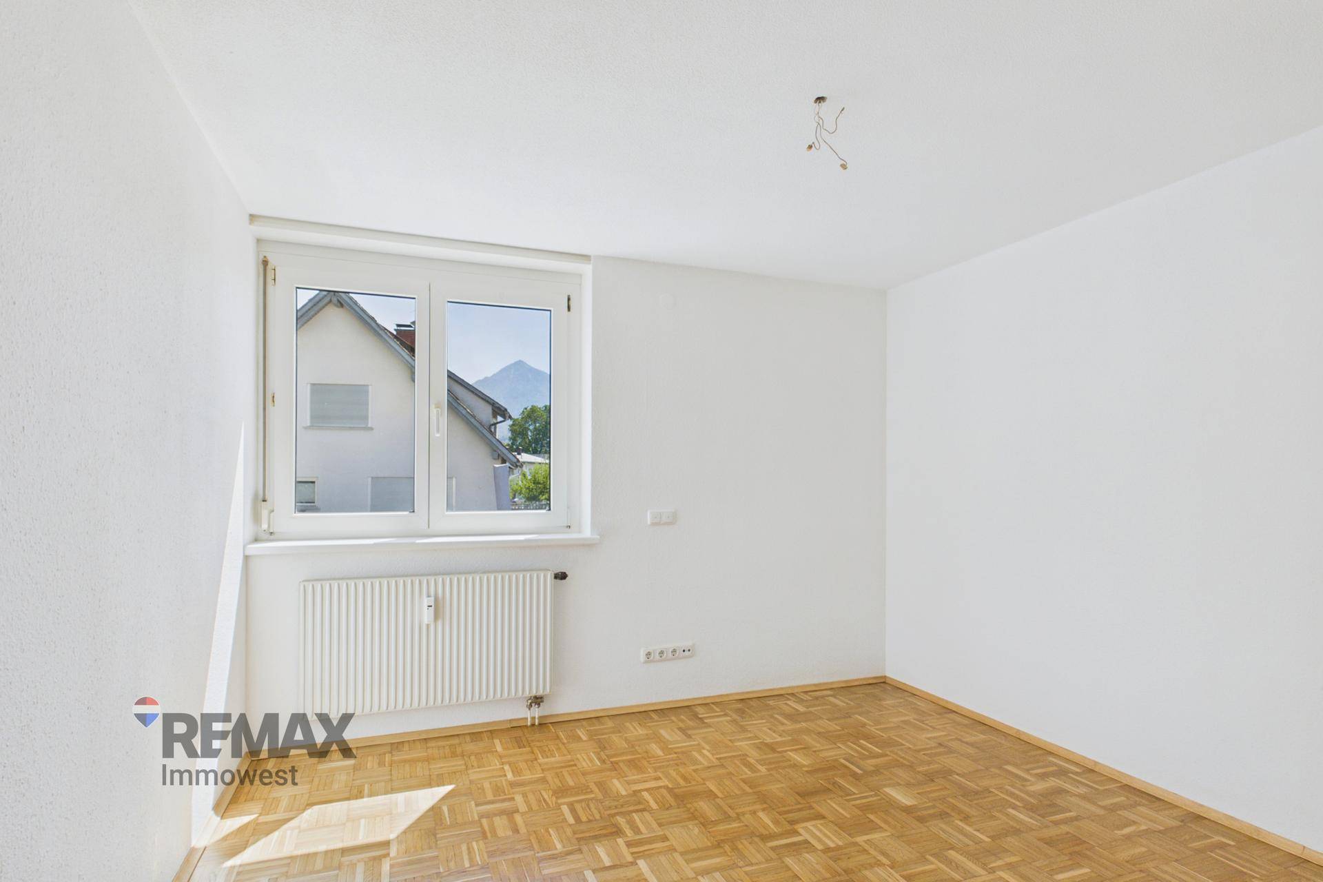 Helles Schlafzimmer mit Parkettboden und Fenster mit Blick auf die Umgebung.