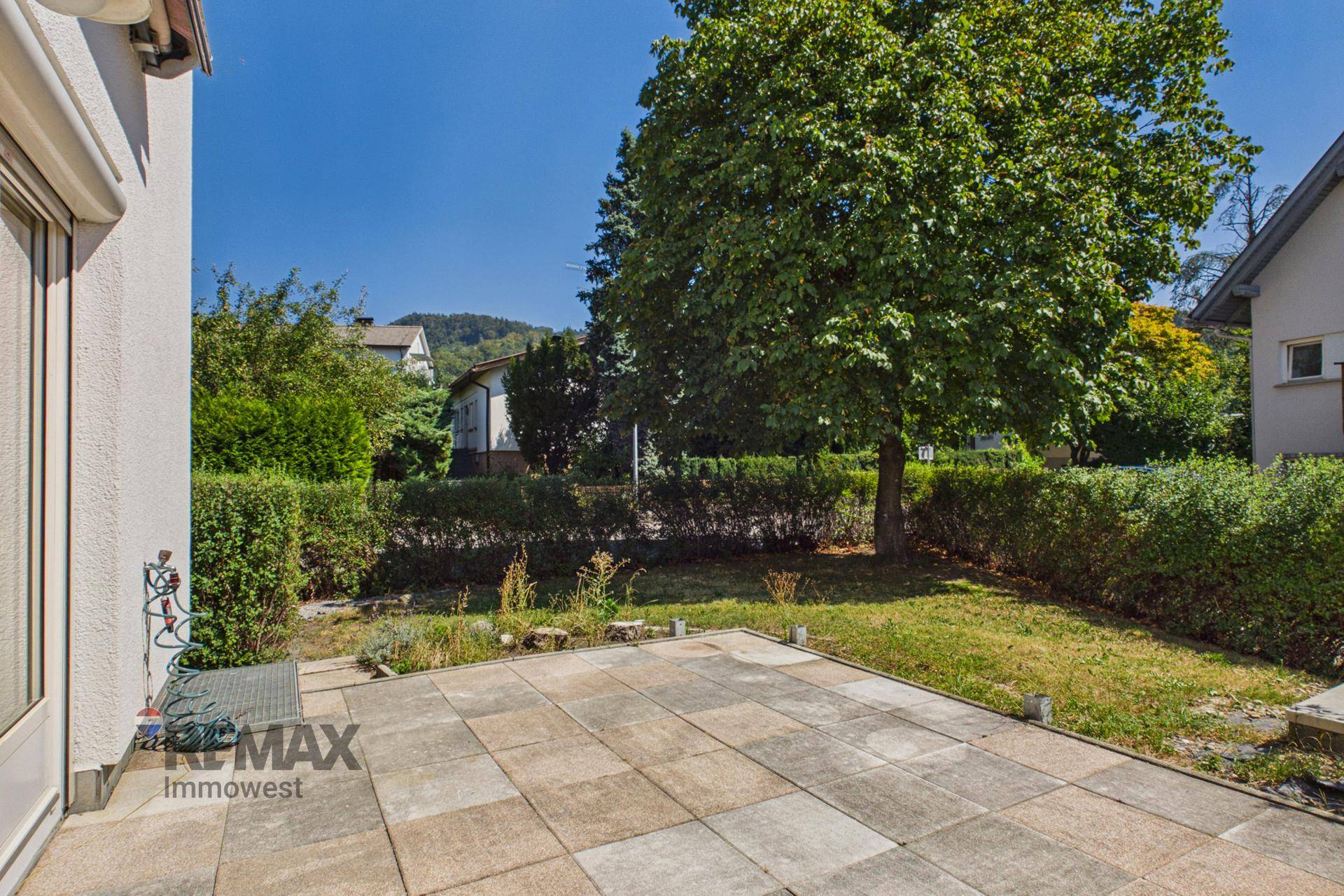 Gepflasterte Terrasse mit Blick auf den grünen Garten und die umliegende Landschaft.