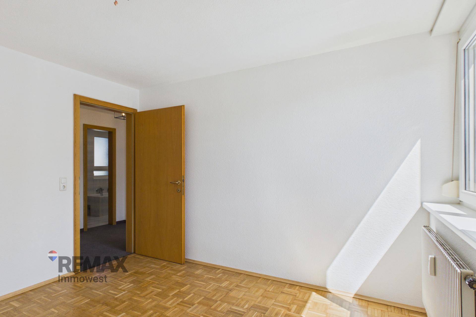 Schlafzimmer mit Parkettboden und Zugang zu einem weiteren Raum, möglicherweise einem Bad.