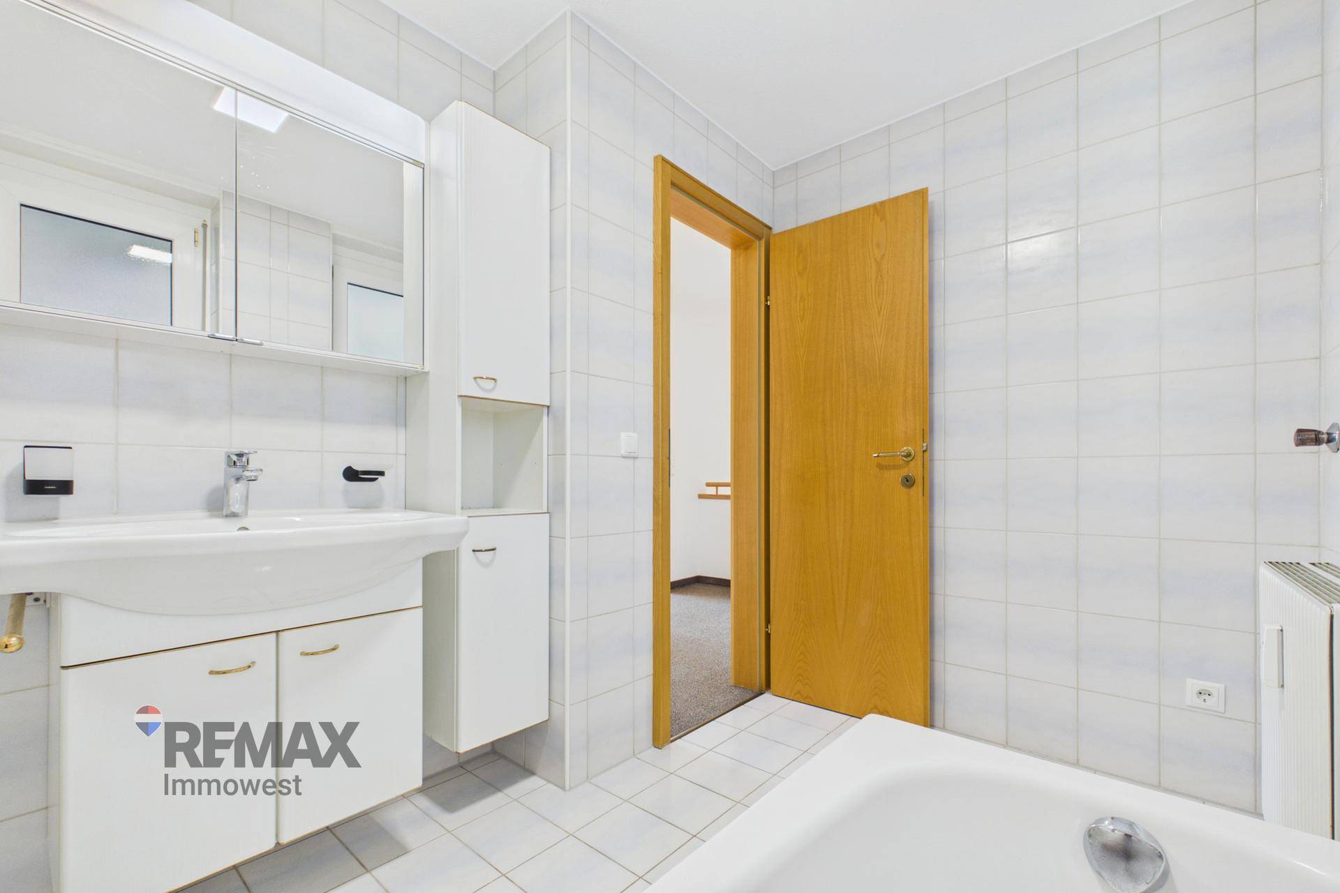 Badezimmer mit Waschbecken, Spiegelschrank und Zugang zum Flur.