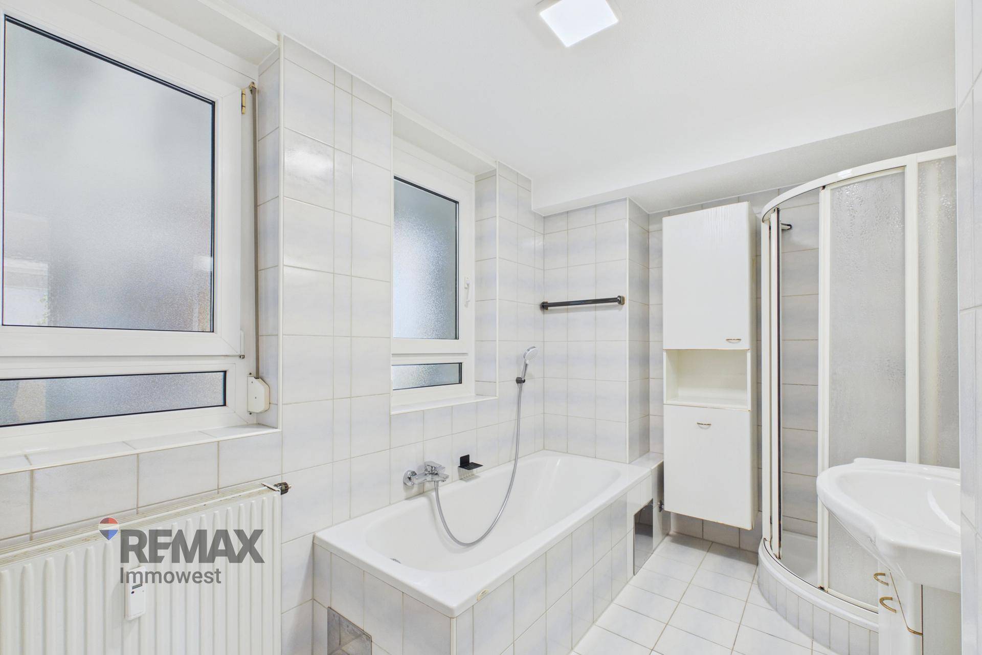 Gefliestes Badezimmer mit Badewanne, Duschkabine und zwei Fenstern für Belüftung.