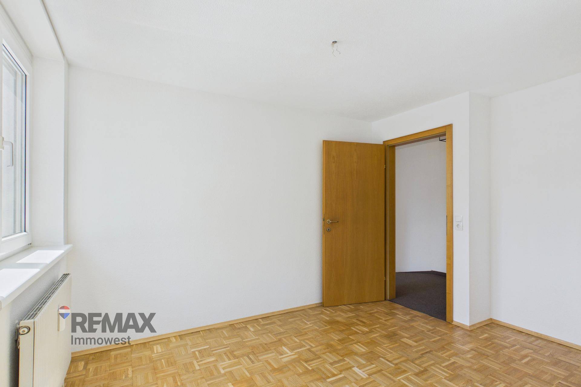 Schlafzimmer mit Parkettboden und Holztür, das einen weiteren Raum erschließt.