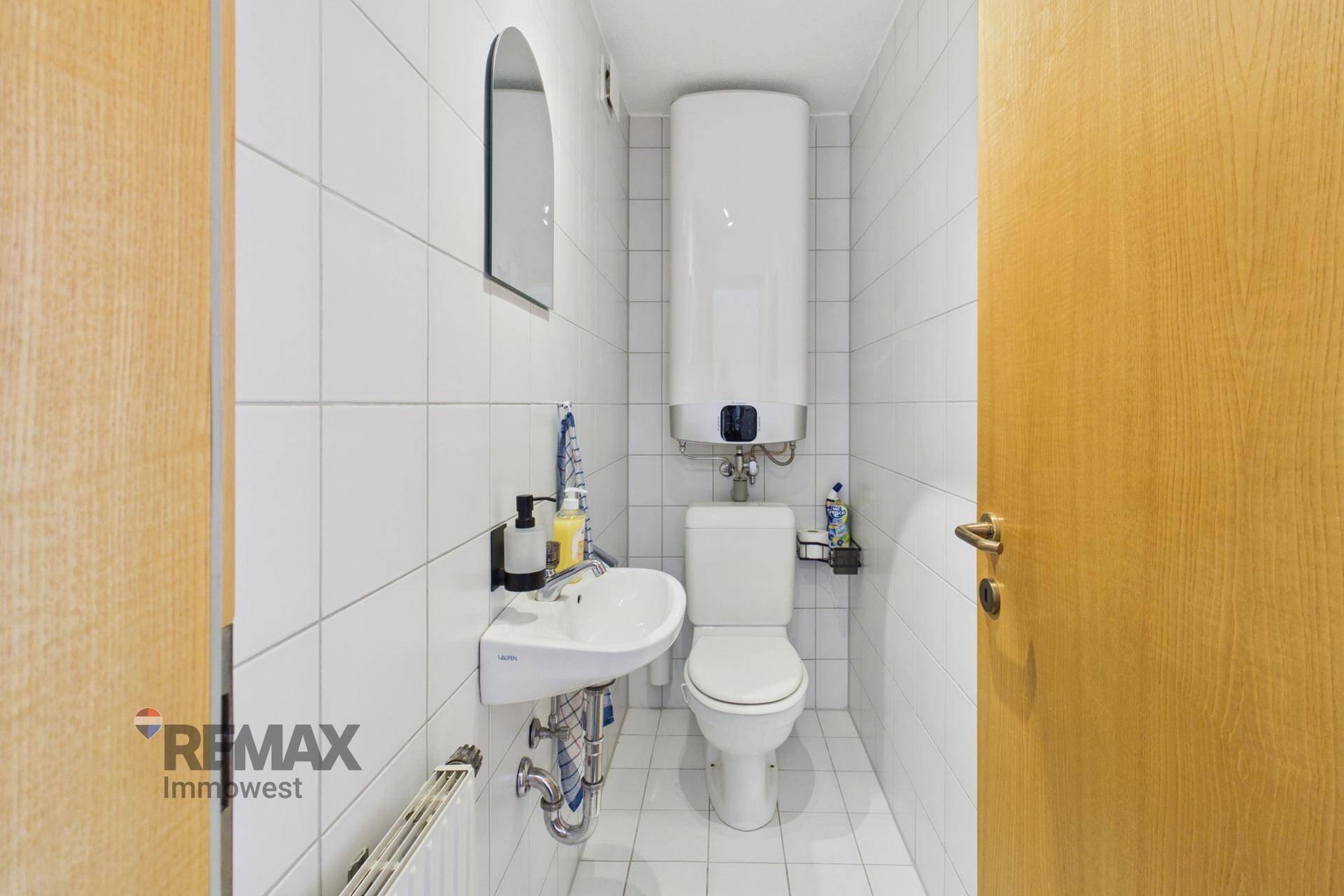 Separates WC mit Waschbecken, Toilette und Wandfliesen in hellem Design.