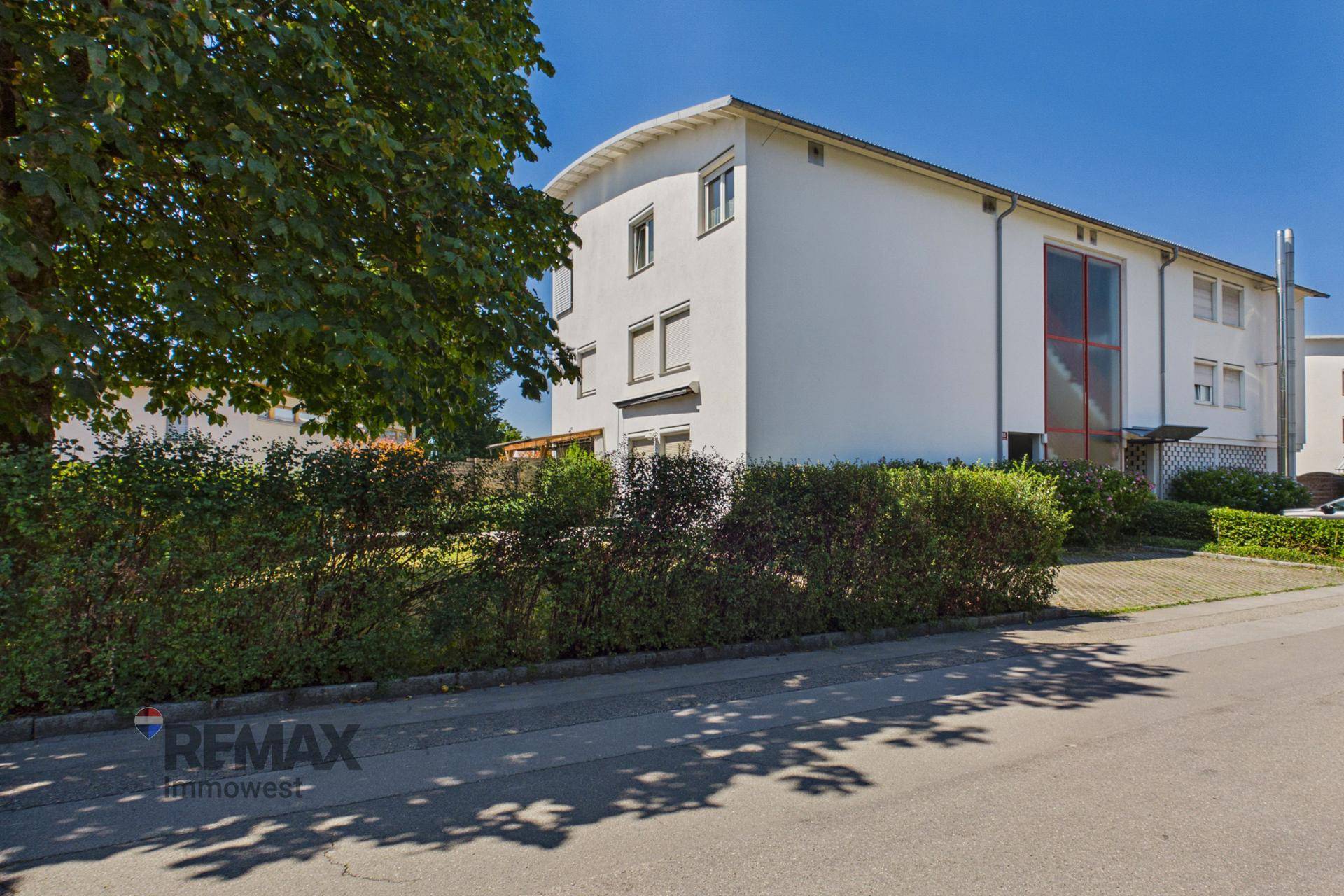 Mehrfamilienhaus mit weißer Fassade und gepflegter Hecke entlang der Straße.