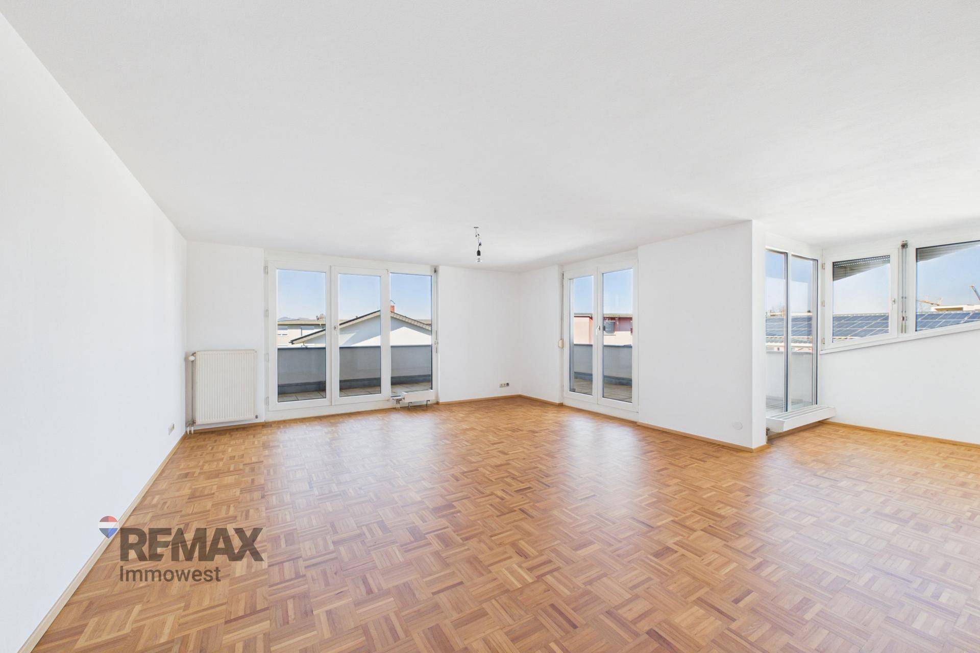 Geräumiger, leerer Wohn-Essbereich mit Fischgrätparkett und mehreren Fenstertüren zum Balkon.
