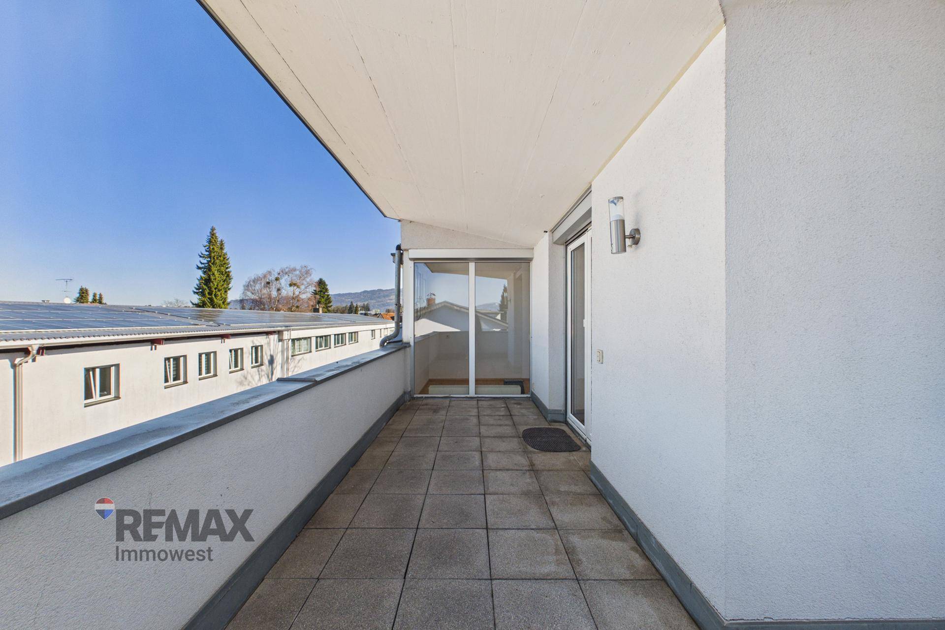 Langer Balkon mit Fliesenboden und Blick auf umliegende Gebäude und Grünflächen.