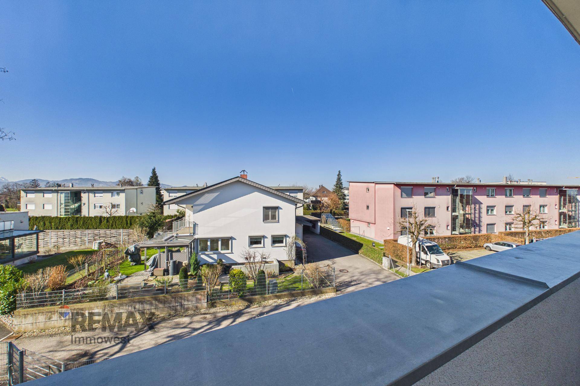 Weitblick vom Balkon über die Nachbarschaft mit Häusern, Bäumen und Bergen im Hintergrund.