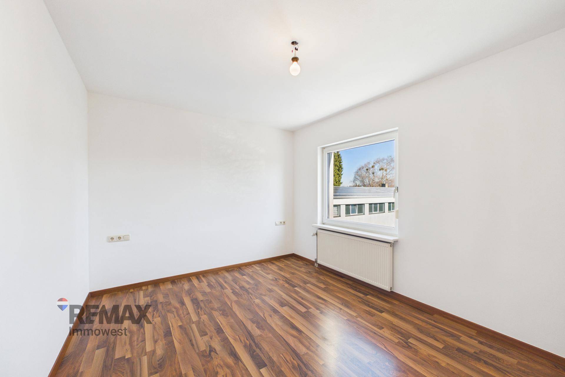 Leeres Schlafzimmer mit Laminatboden und einem Fenster, das viel Tageslicht hereinlässt.