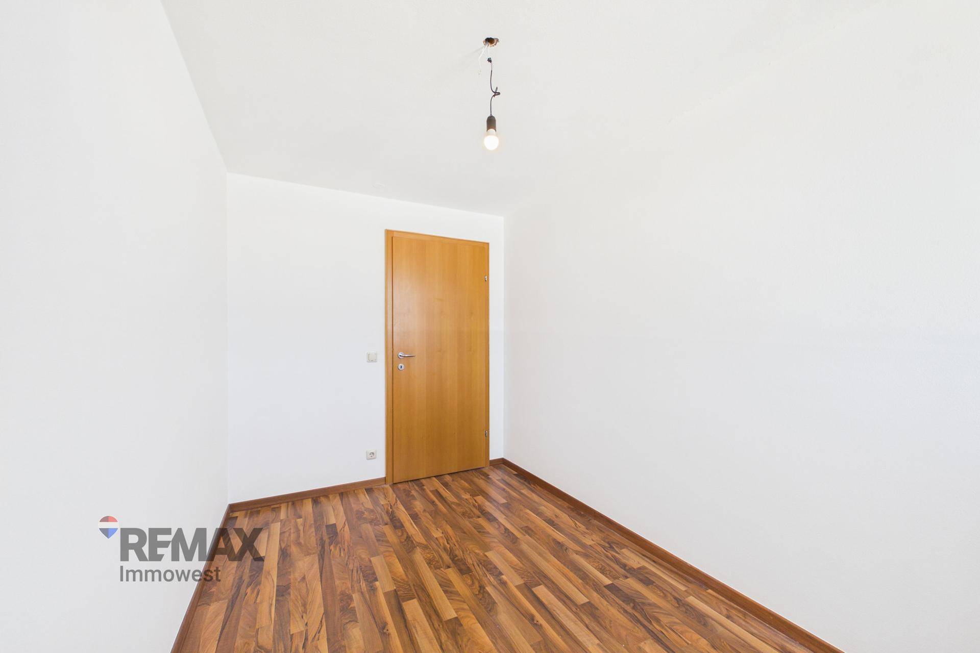 Leeres Zimmer mit Laminatboden und Holztür, bietet flexible Nutzungsmöglichkeiten.
