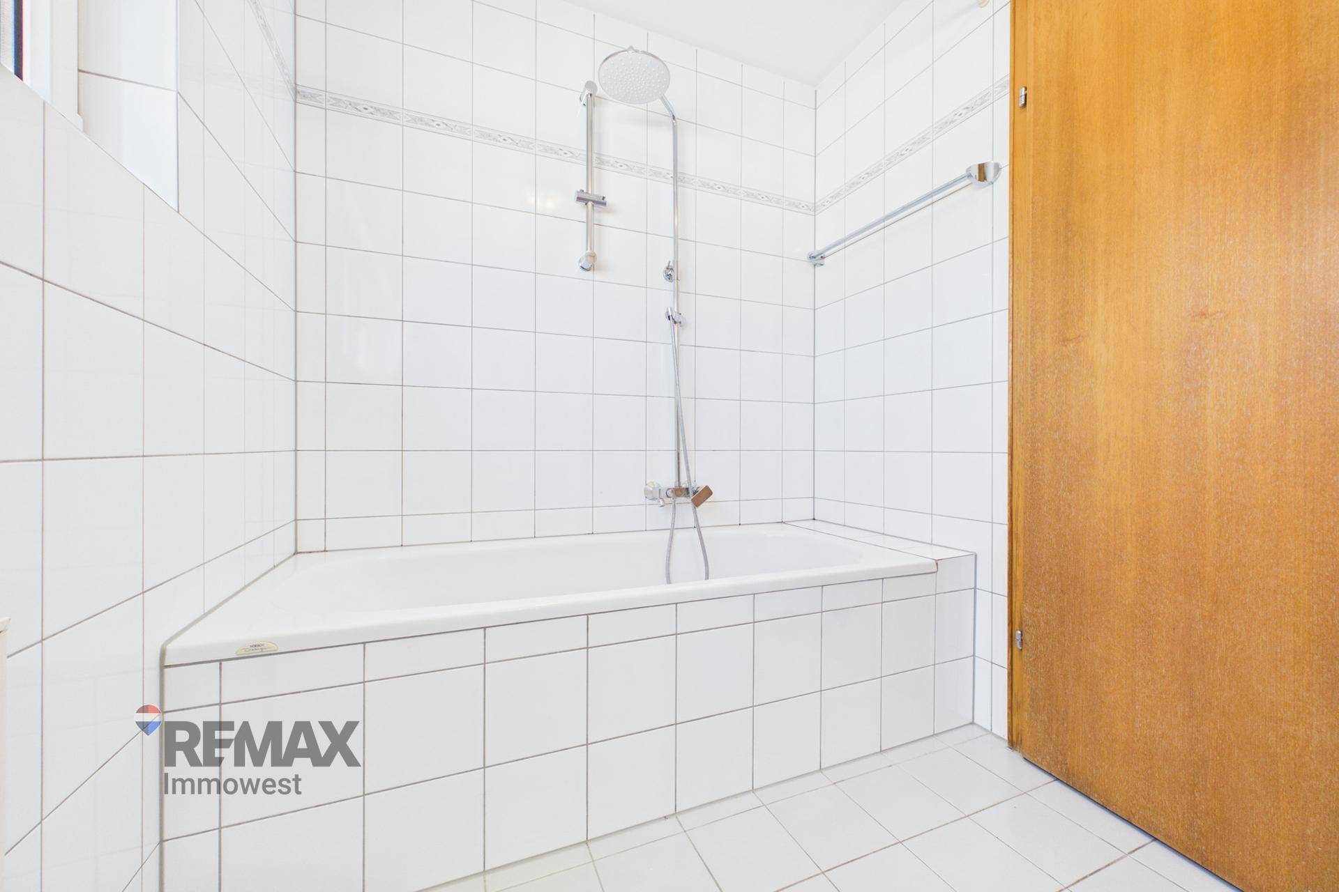 Badezimmer mit weiß gefliester Badewanne und Duschvorrichtung, funktional und sauber.