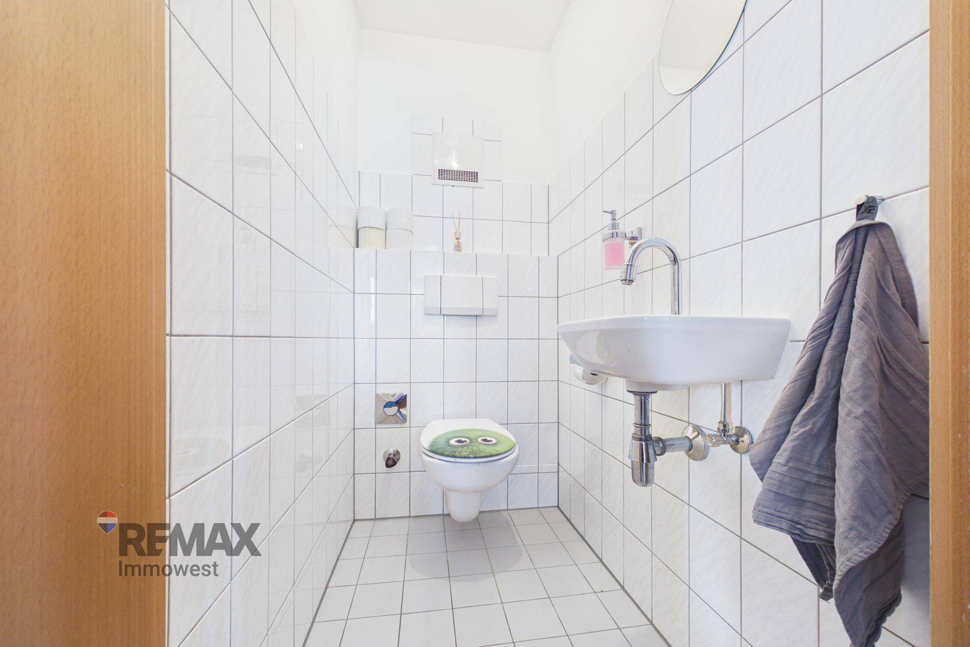 Kleines Gäste-WC mit weißen Fliesen, Toilette und Handwaschbecken, praktisch und hell.