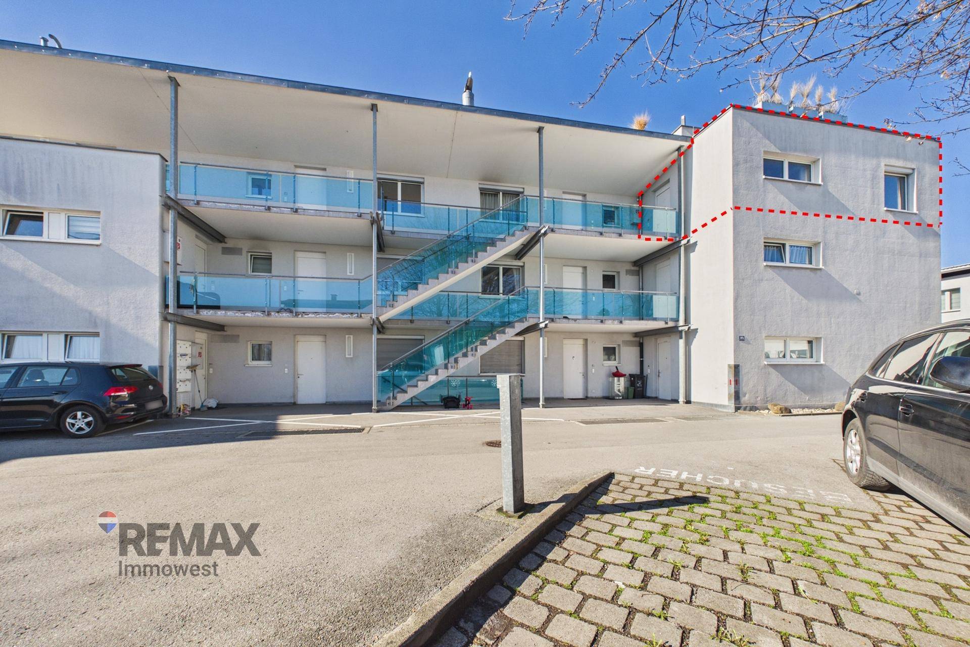 Rückansicht des Mehrfamilienhauses mit Balkonen, Außentreppen und Parkplätzen.