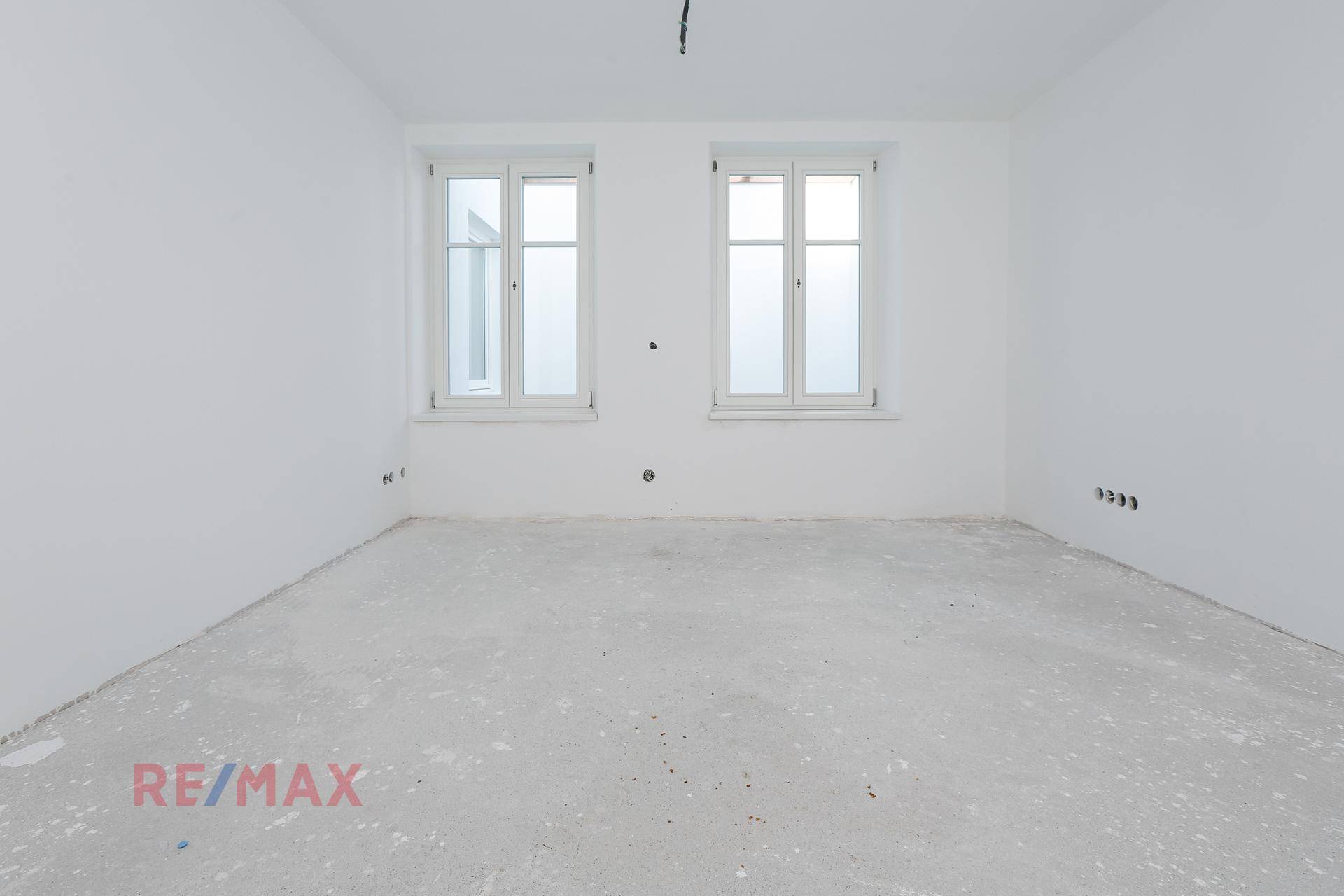 Leerer Raum im Rohbau mit weißen Wänden und zwei Fenstern, bereit für den Innenausbau und Gestaltung.