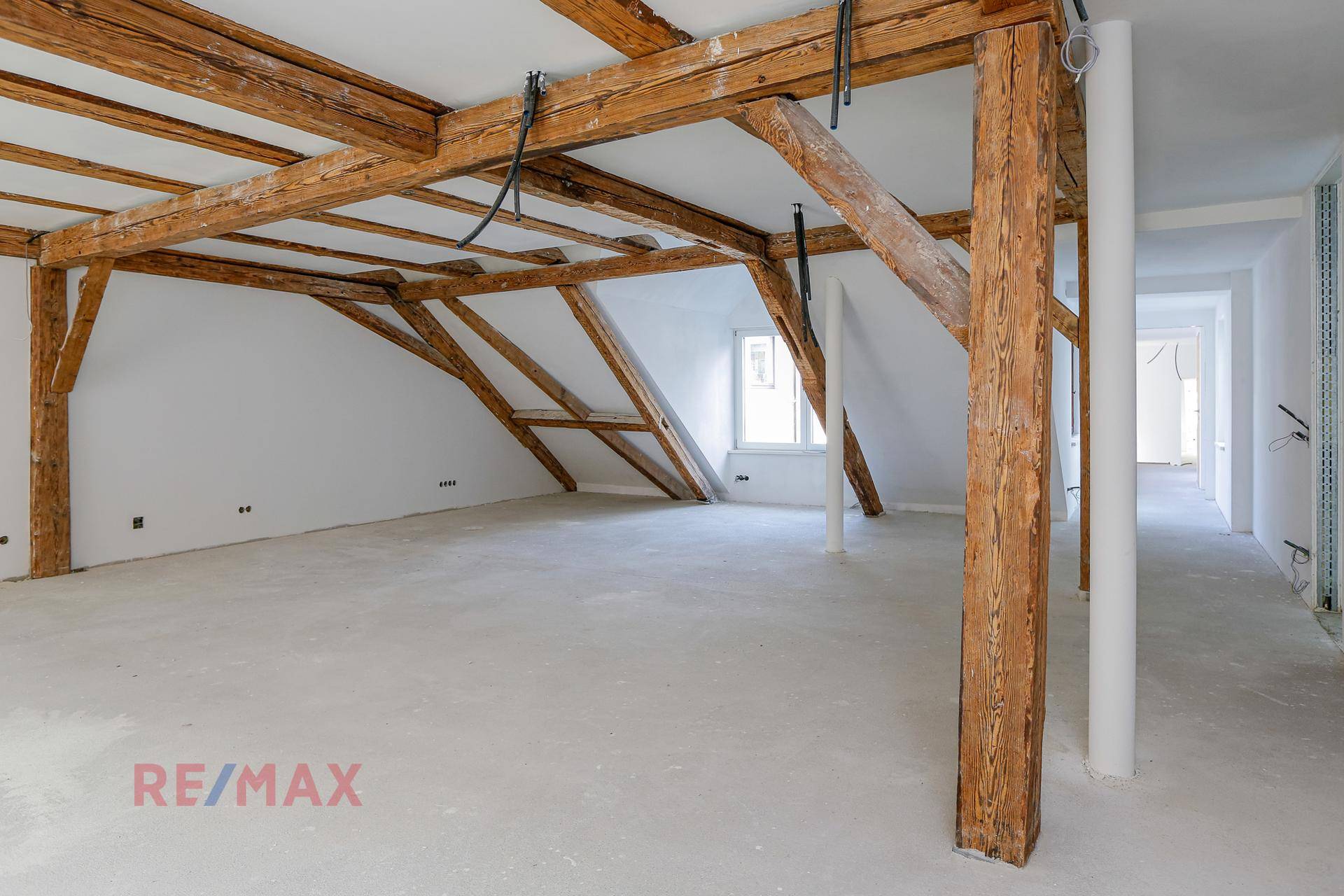 Geräumiger Dachboden im Rohbau mit sichtbaren Holzbalken und einem Fenster, bereit zum individuellen Ausbau.