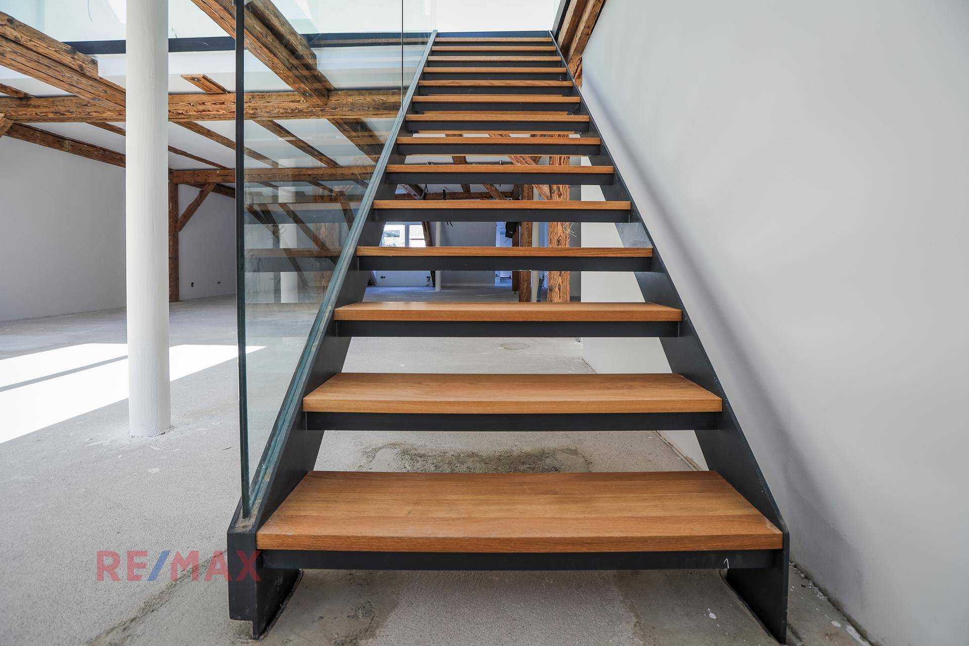 Moderne Treppe mit Holzstufen und Glasgeländer, die verschiedene Ebenen des Dachgeschosses verbindet.