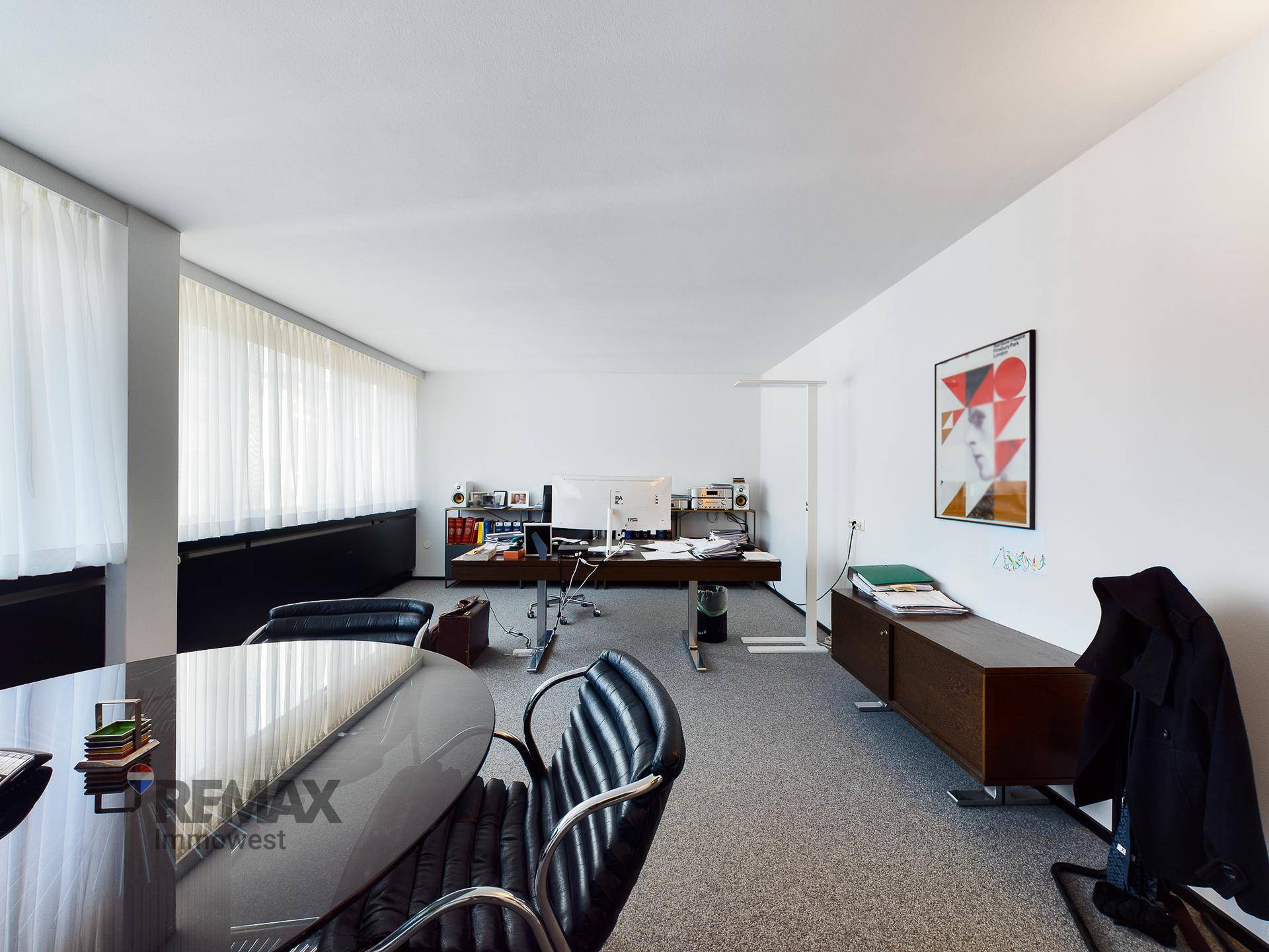 Großes Büro mit mehreren Arbeitsplätzen, Teppichboden und viel Tageslicht durch die Fenster.