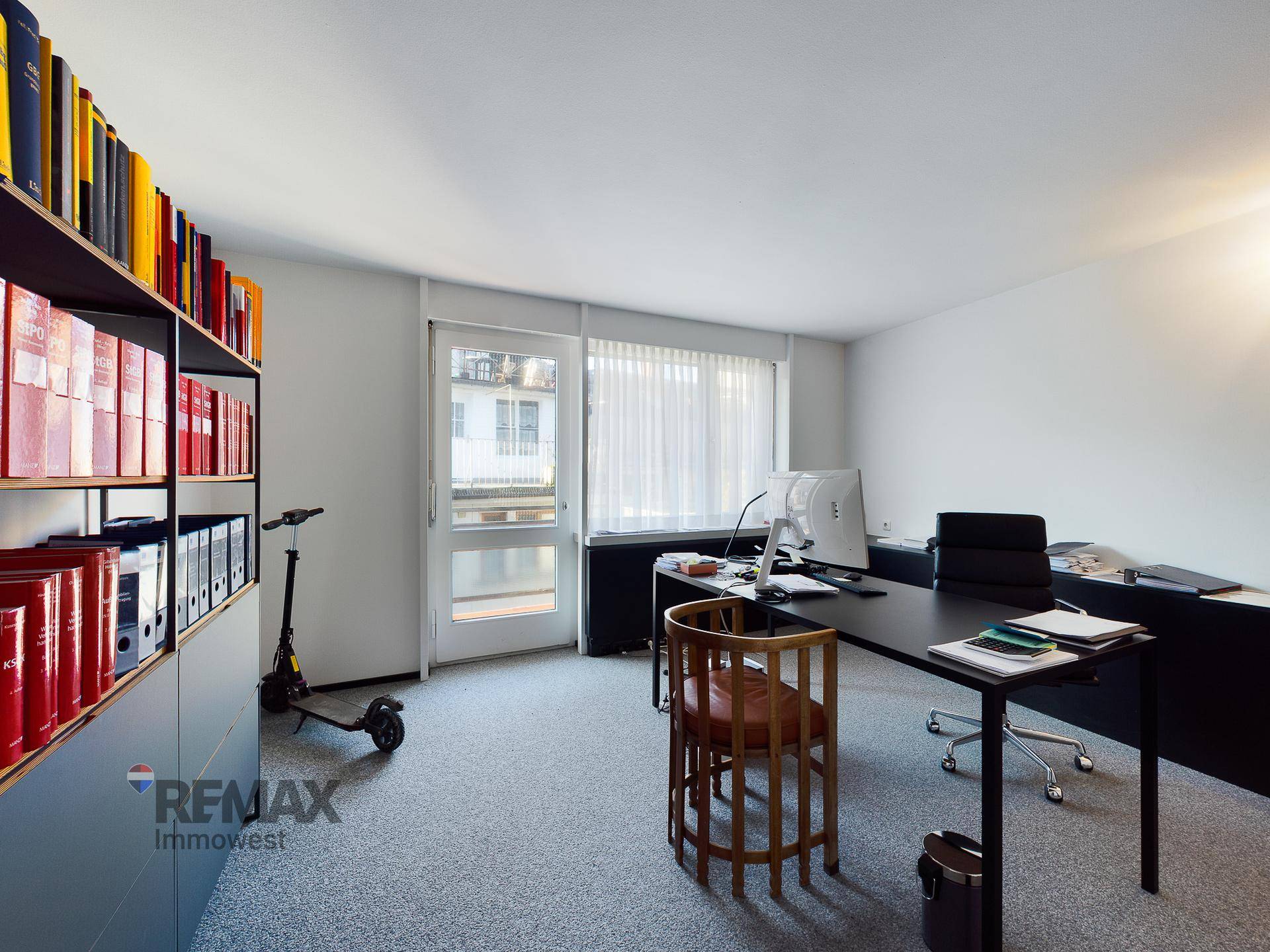 Büro mit Bücherregal, Schreibtisch und Zugang zu einem Balkon durch eine Fenstertür.